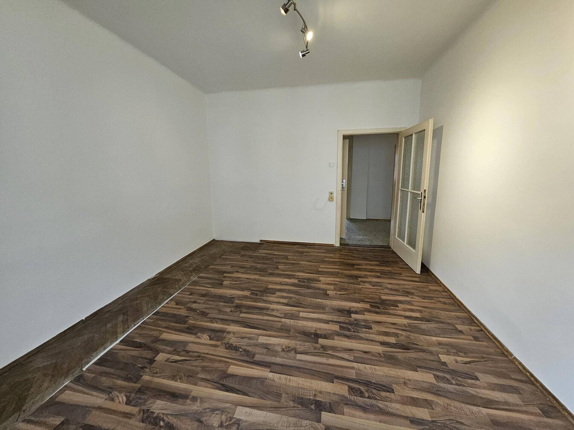 Geräumiges Zimmer mit Laminatboden und einer Tür, die zu einem weiteren Raum führt.
