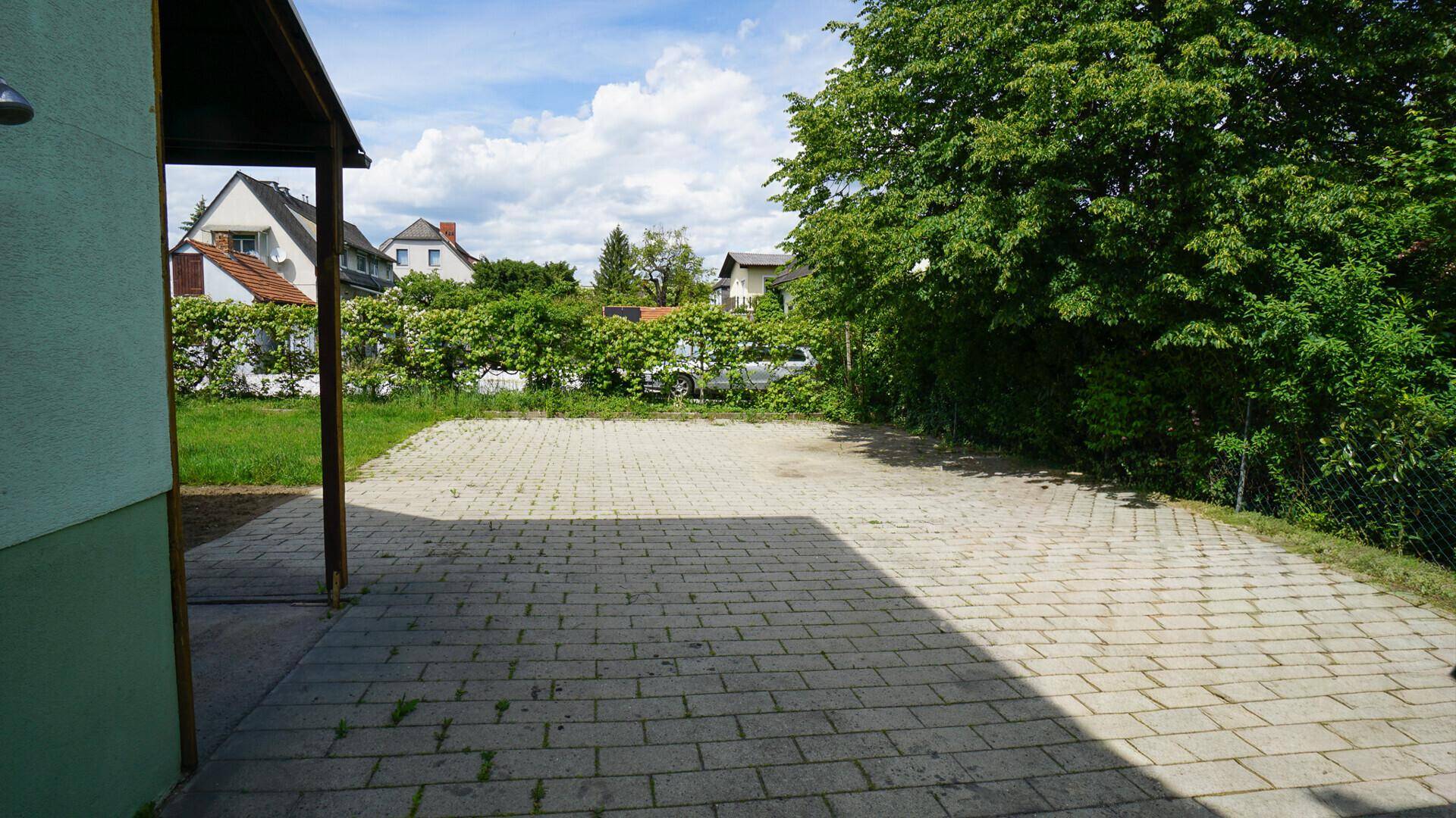 Gepflasterter Außenbereich neben dem Haus, umgeben von Bäumen und einer Hecke.