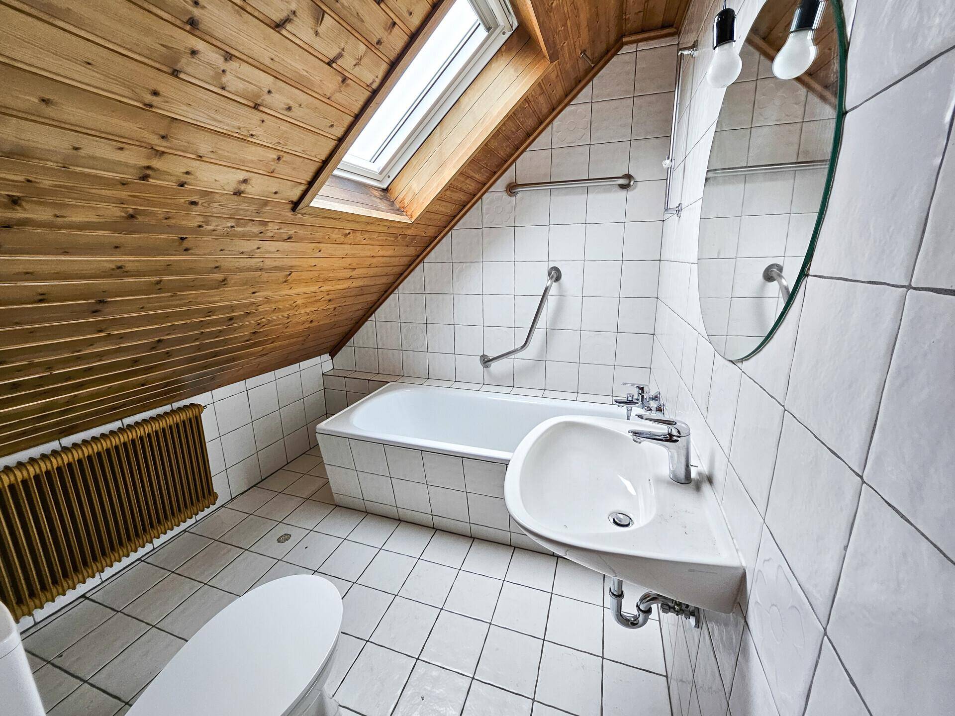 Badezimmer im Dachgeschoss mit Badewanne, Dachfenster, Fliesen und Haltegriffen.