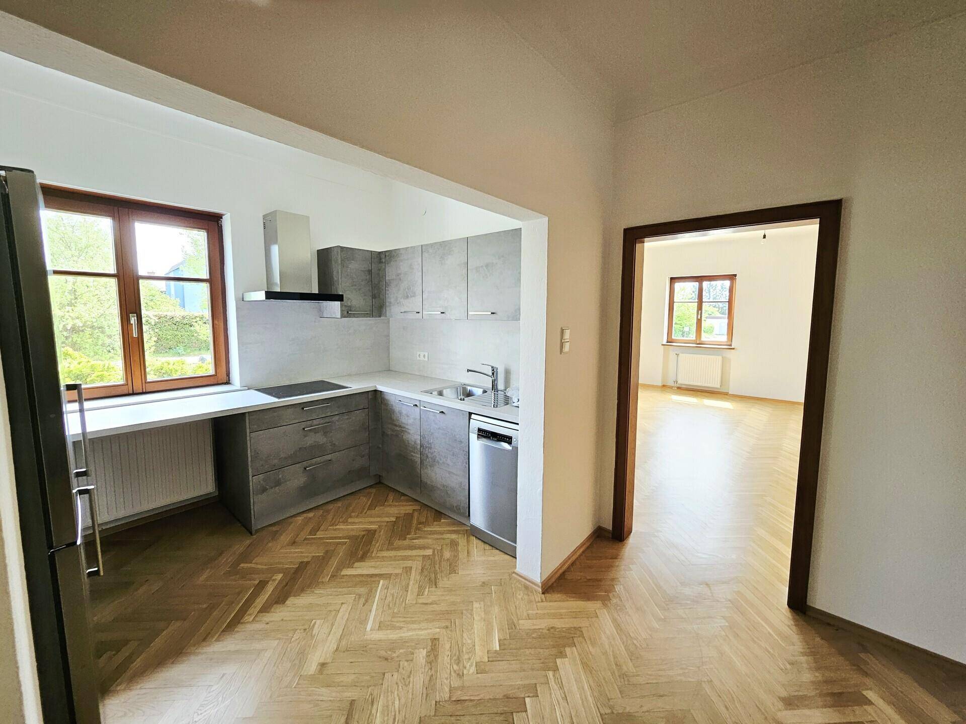 Offene Küche mit modernen grauen Schränken, Spülmaschine und einem Fenster mit Blick ins Grüne.