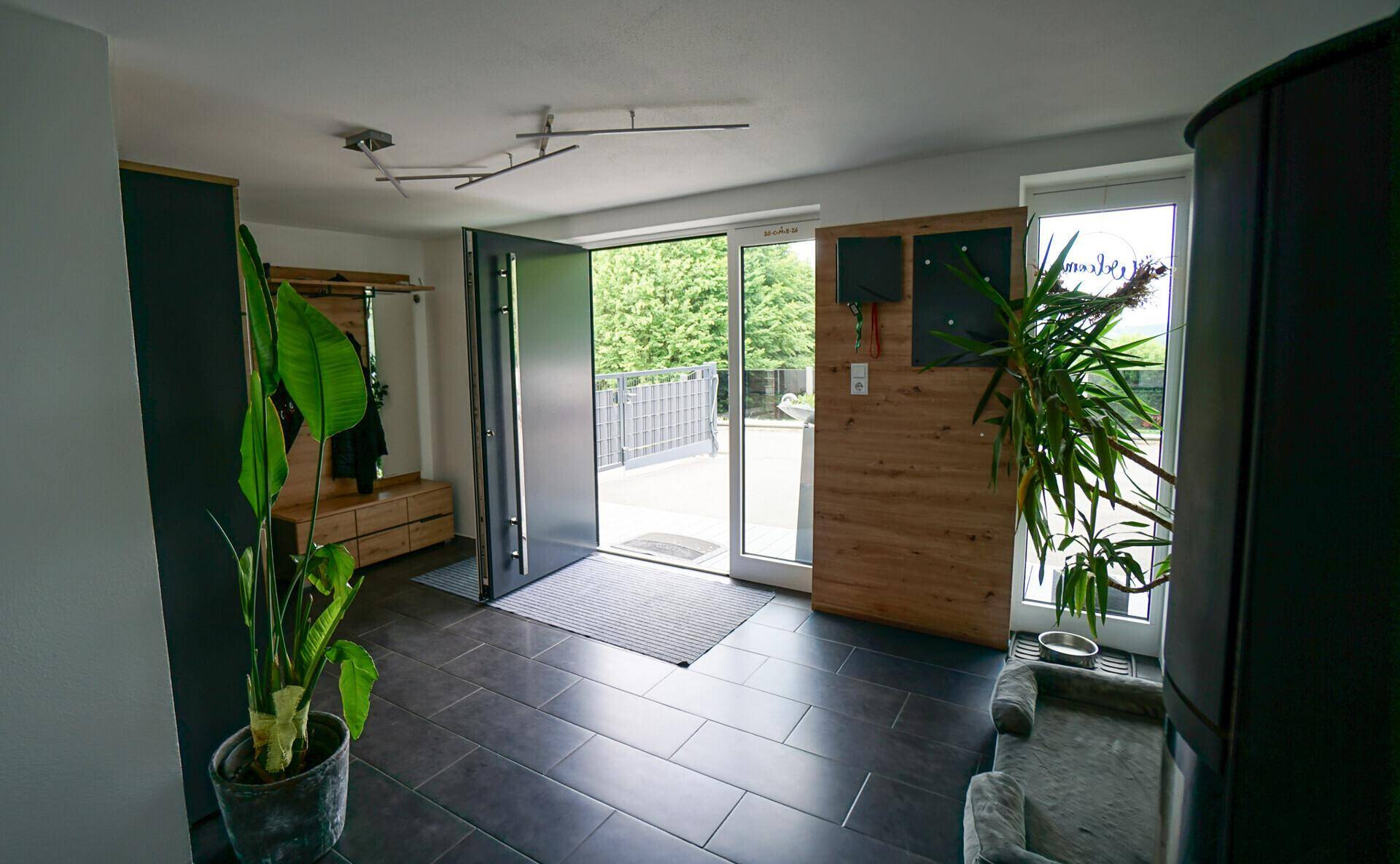 Moderner Eingangsbereich mit dunklen Fliesen, Garderobe und viel Tageslicht.