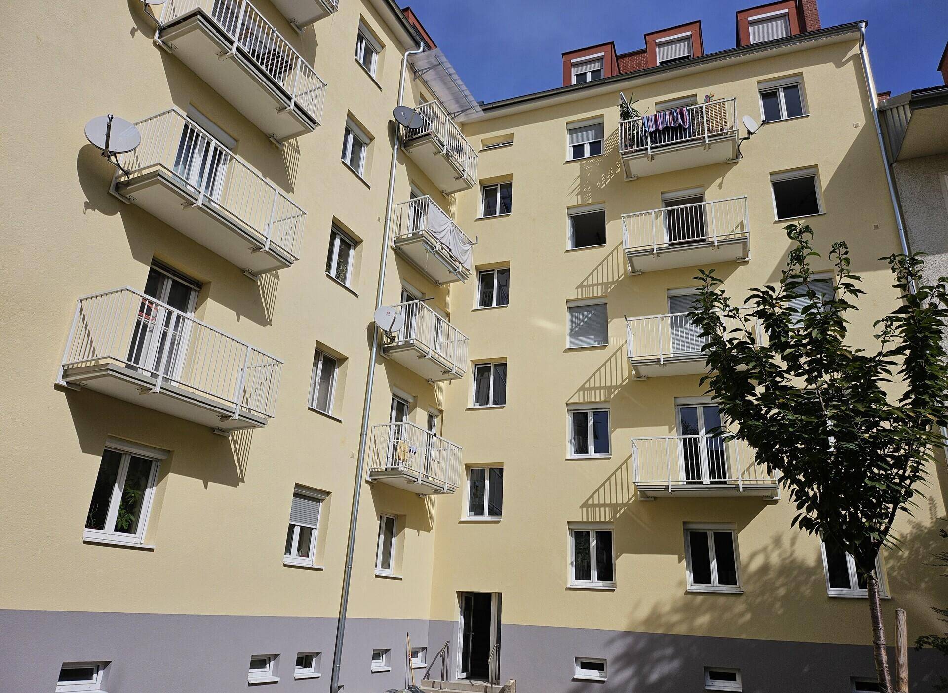 Rückansicht eines Mehrfamilienhauses mit vielen Balkonen und Satellitenschüsseln an der Fassade.