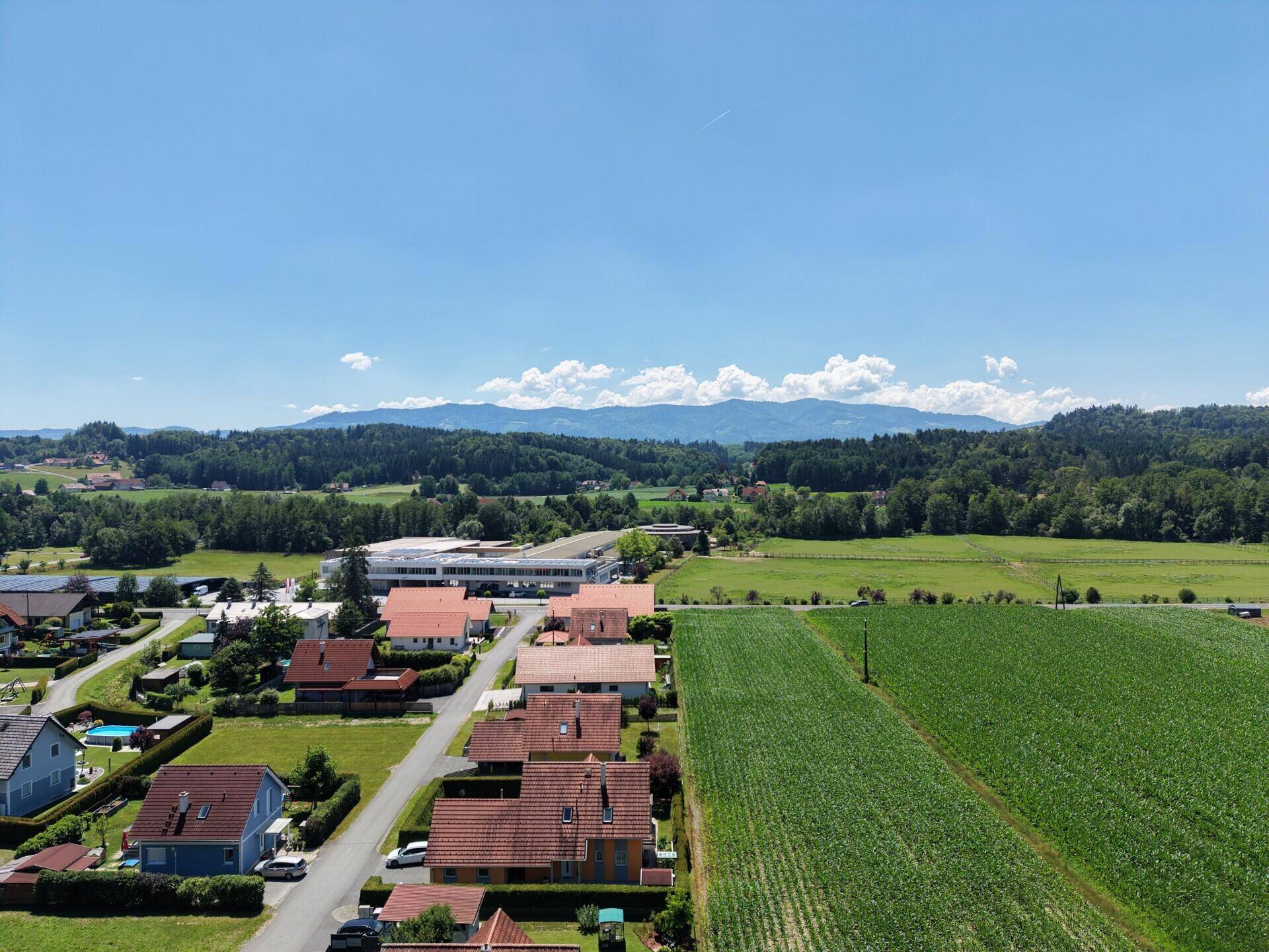 Weitläufige Luftaufnahme der ländlichen Umgebung mit Feldern und Bergen im Hintergrund.