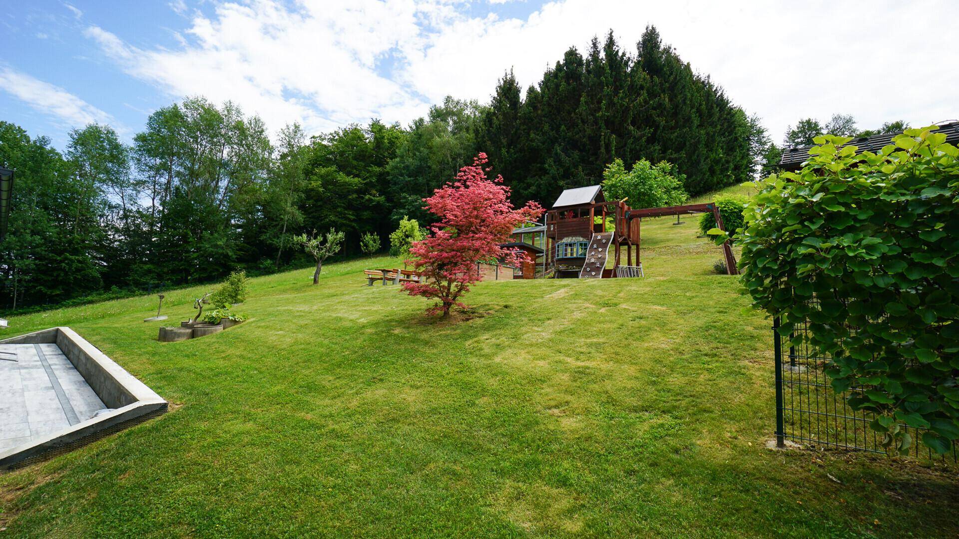 Großer Spielplatz mit Rutsche und Schaukel im weitläufigen, grünen Gartenbereich des Anwesens.