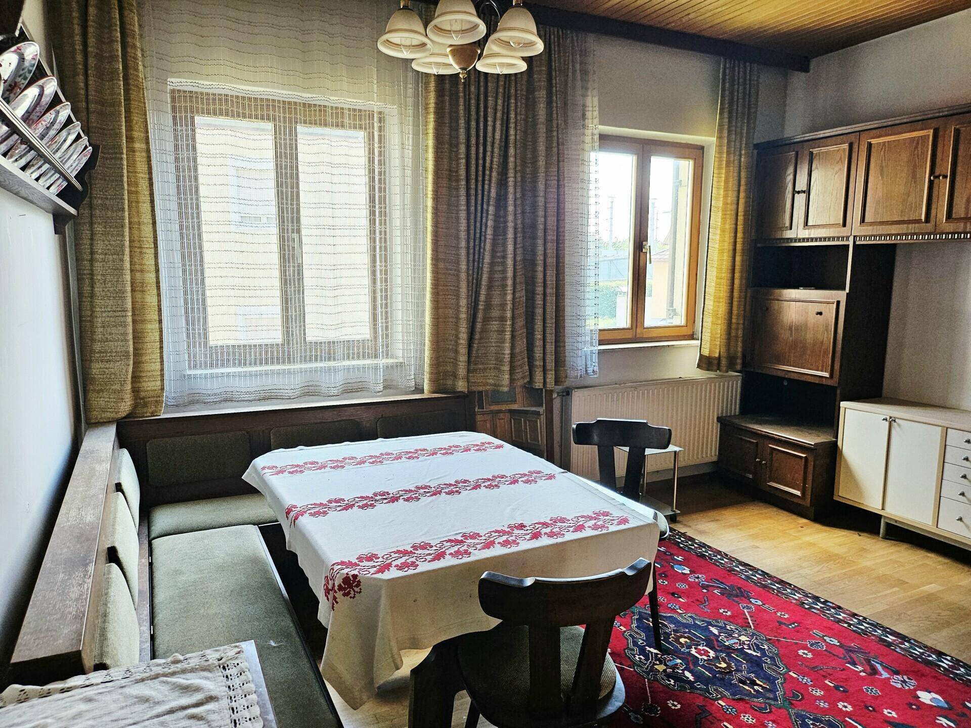 Gemütlicher Essbereich mit traditionellen Holzmöbeln, Teppich und zwei Fenstern.