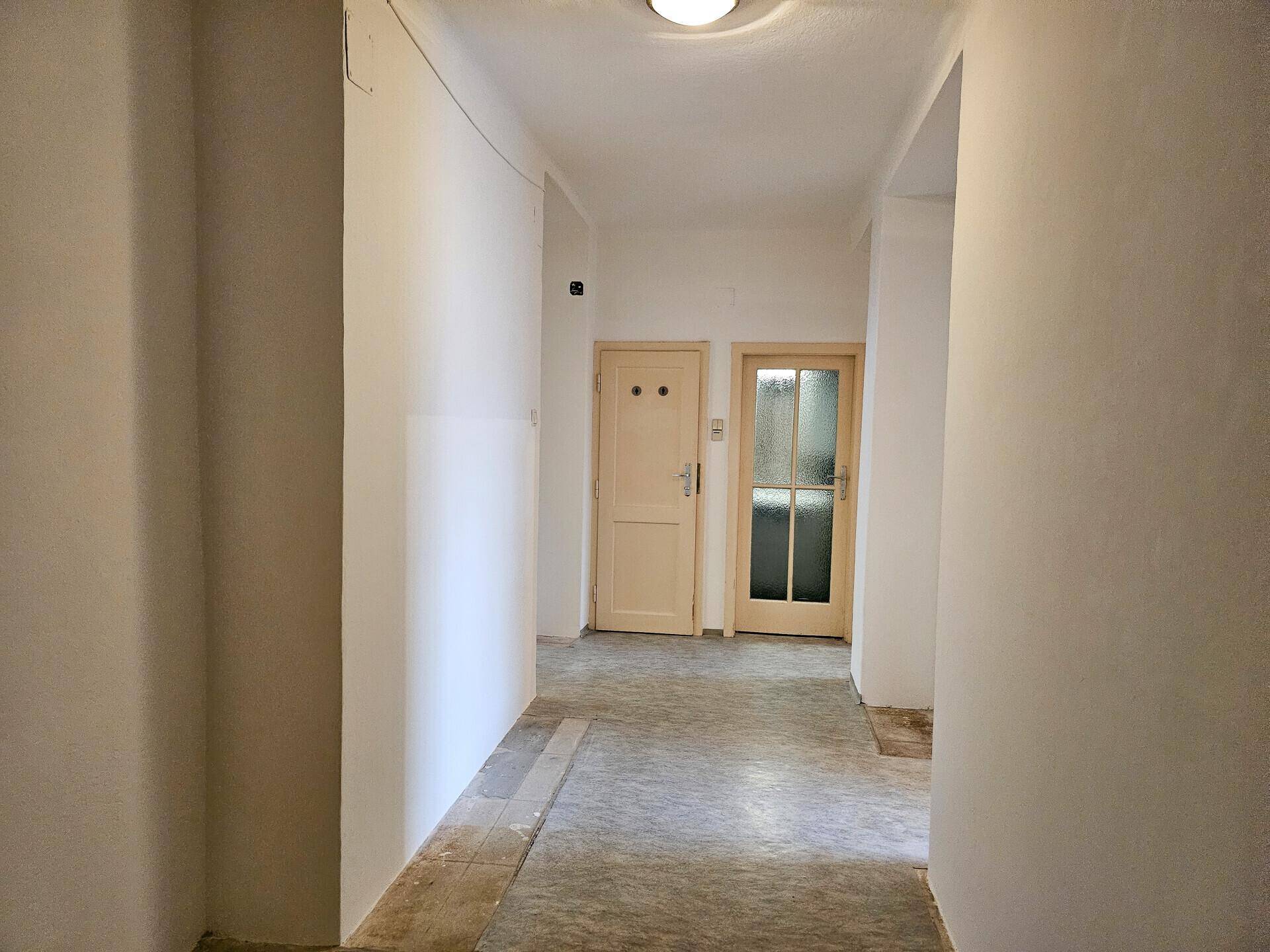 Langer Flur mit hellen Wänden und Türen zu verschiedenen Zimmern, mit Renovierungsbedarf.