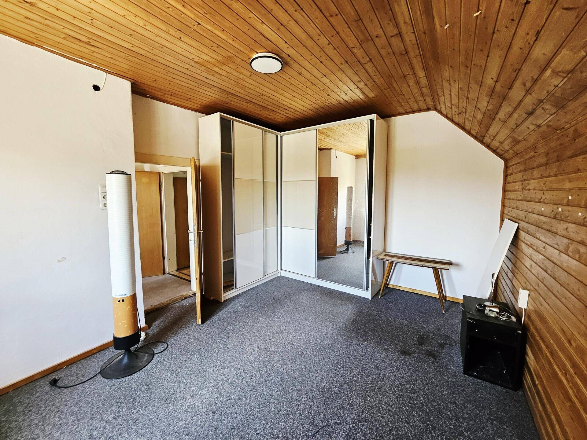 Dachzimmer mit Teppichboden, Holzvertäfelung und einem großen Spiegelschrank.