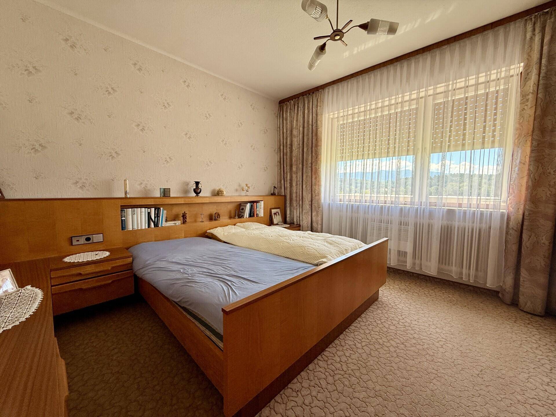 Helles Schlafzimmer mit Doppelbett, Nachttischen und einem großen Fenster mit Vorhängen.