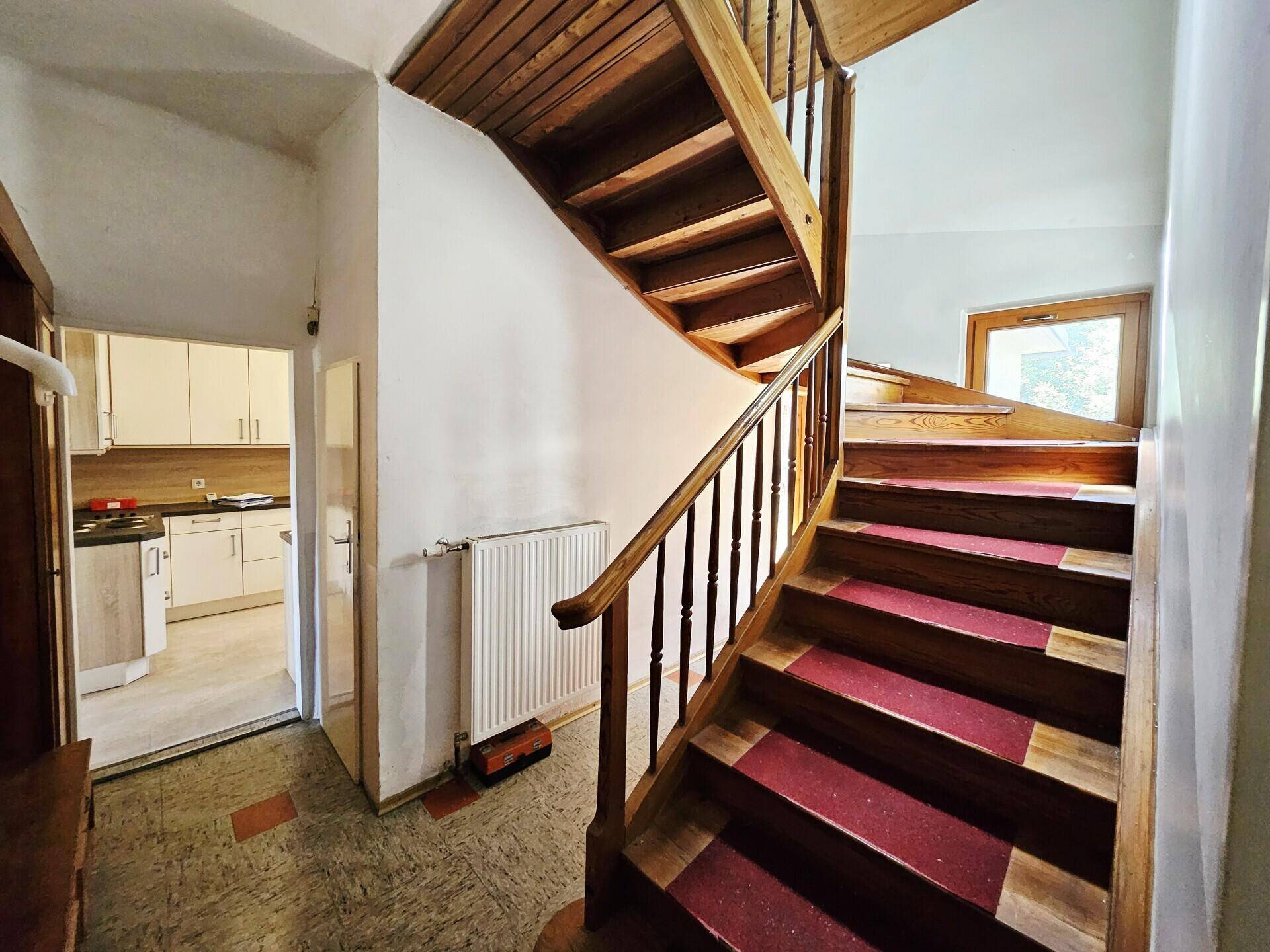 Treppenhaus mit Holzstufen und rotem Teppich, führt zu den oberen Etagen.