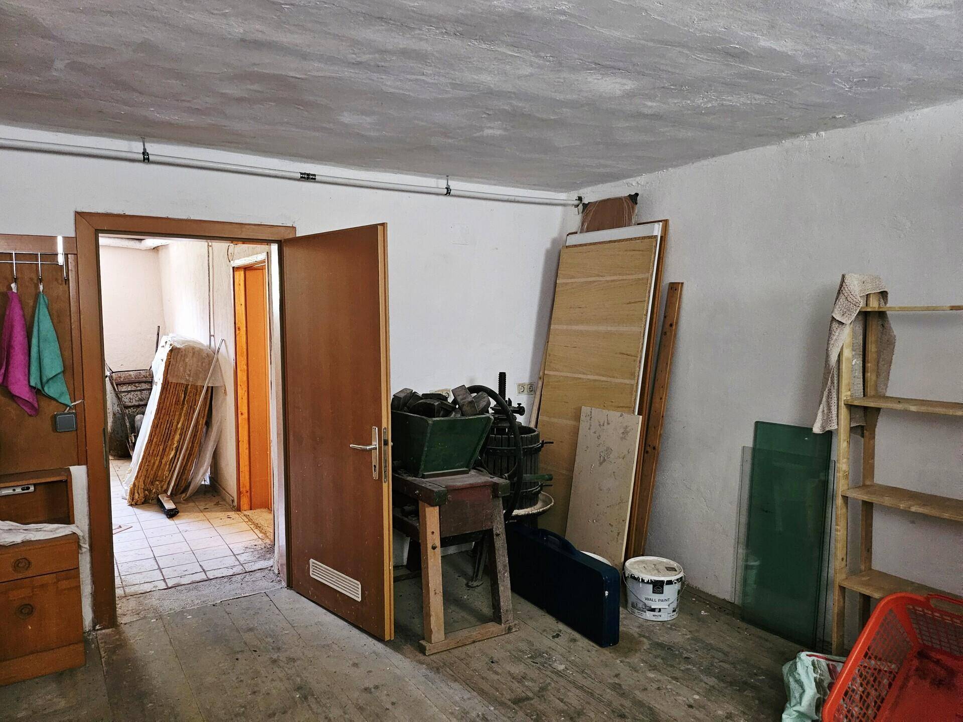 Durchgang zwischen zwei Kellerräumen mit unterschiedlichen Bodenbelägen und Lagerflächen, funktional eingerichtet.