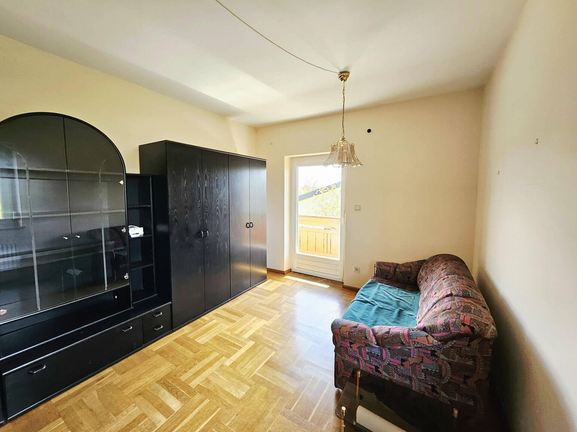 Zimmer mit Parkettboden, dunklen Möbeln und Zugang zu einem kleinen Balkon.