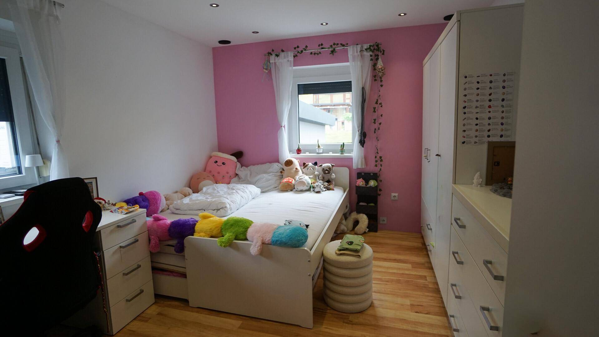 Helles Kinderzimmer mit rosa Wand, Holzfußboden und vielen Stofftieren, ideal für junge Bewohner.