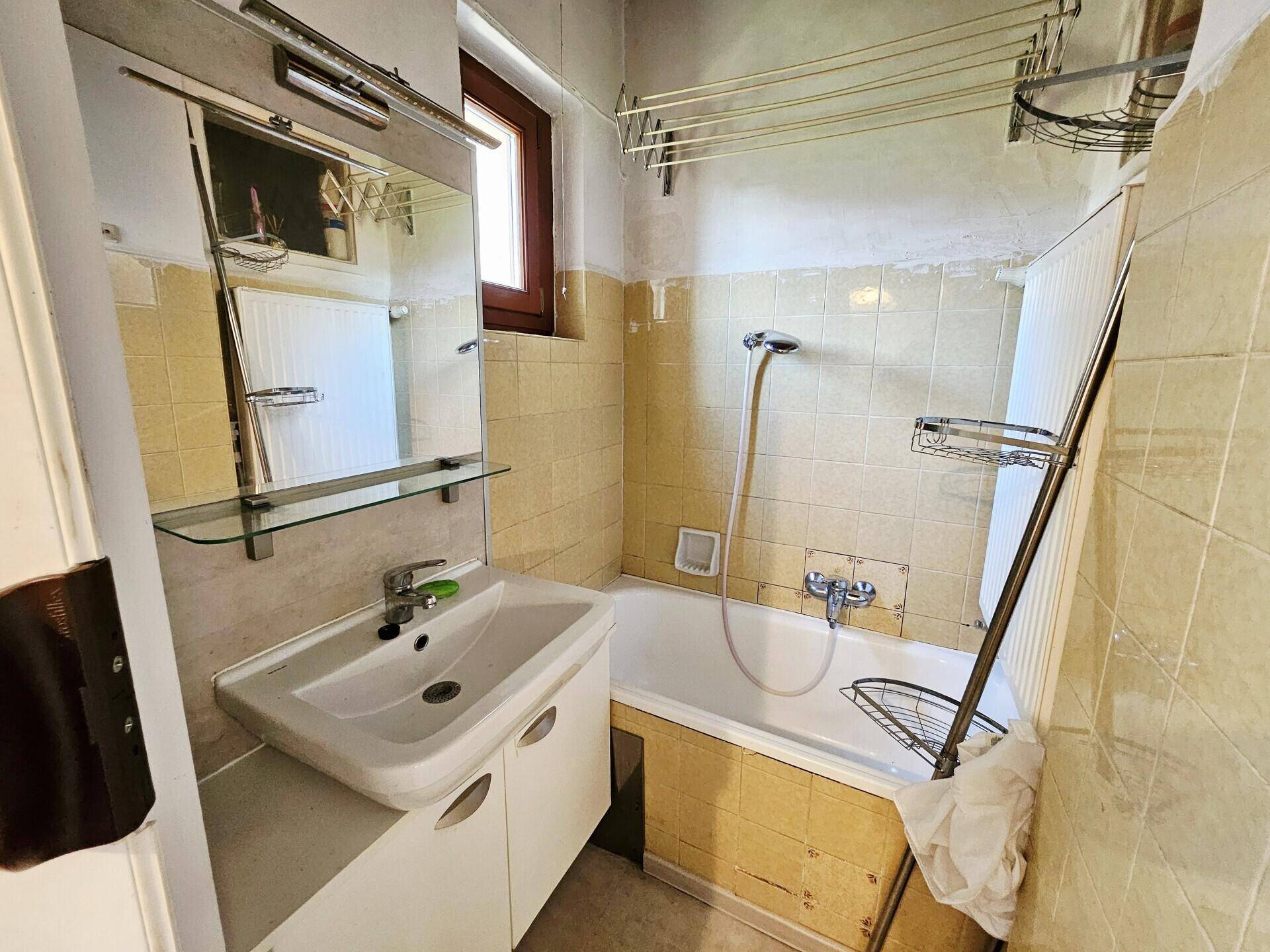 Badezimmer mit gelben Fliesen, Badewanne, Waschbecken und einem Fenster für Tageslicht.