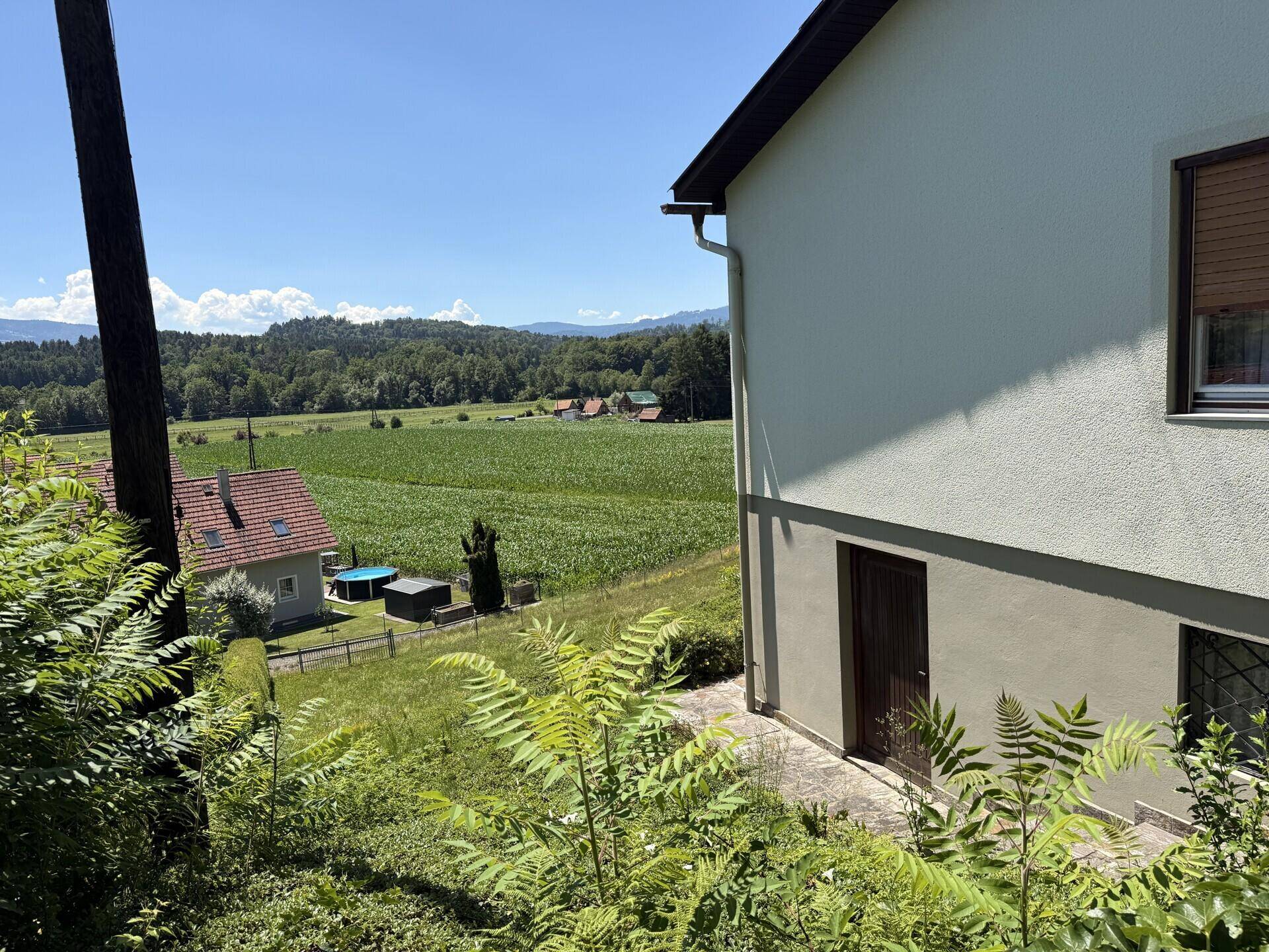 Seitenansicht des Hauses mit Blick auf weite Felder und die umliegende grüne Landschaft.
