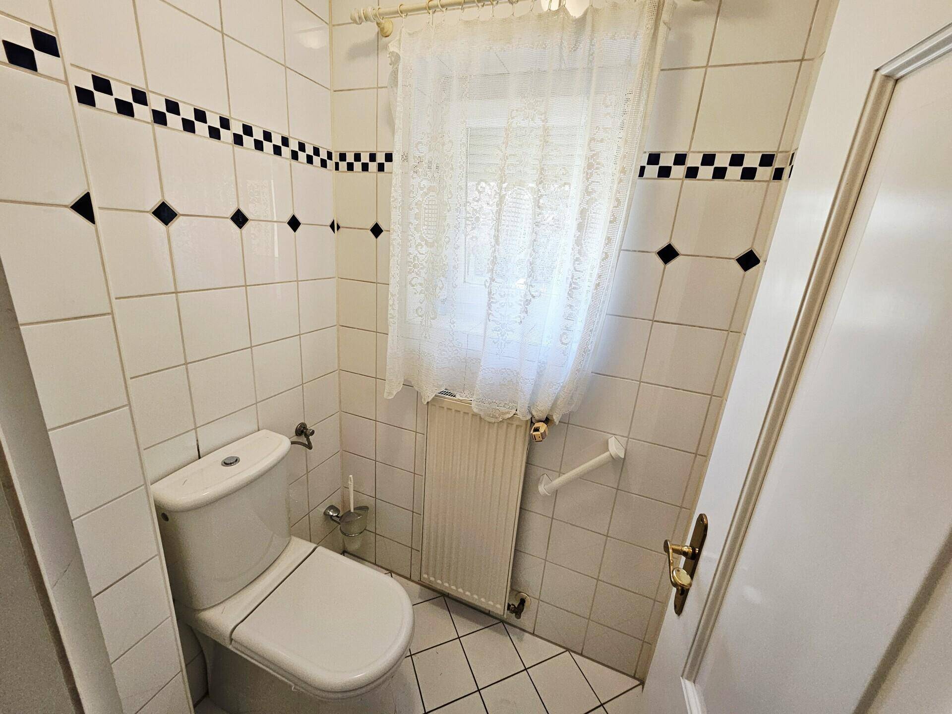 Separate Toilette mit Wand-WC, Heizkörper und Haltegriffen für Barrierefreiheit.