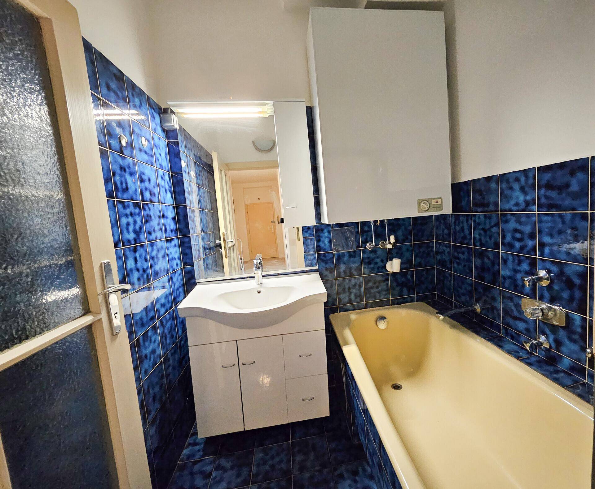 Badezimmer mit blauen Fliesen, Badewanne, Waschbecken und Spiegelschrank.