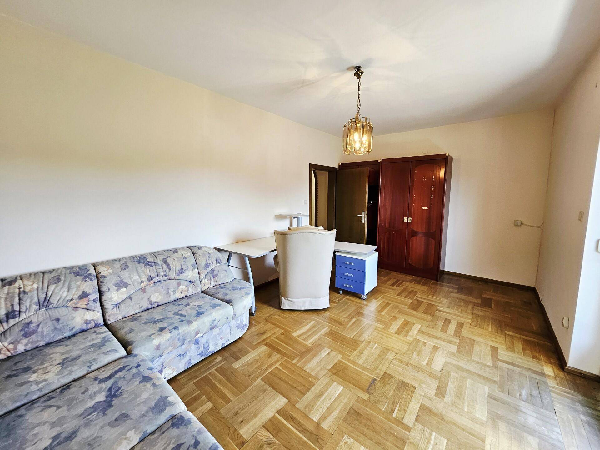 Geräumiges Zimmer mit Parkettboden, Sofa und Schreibtisch, ideal als Gästezimmer.