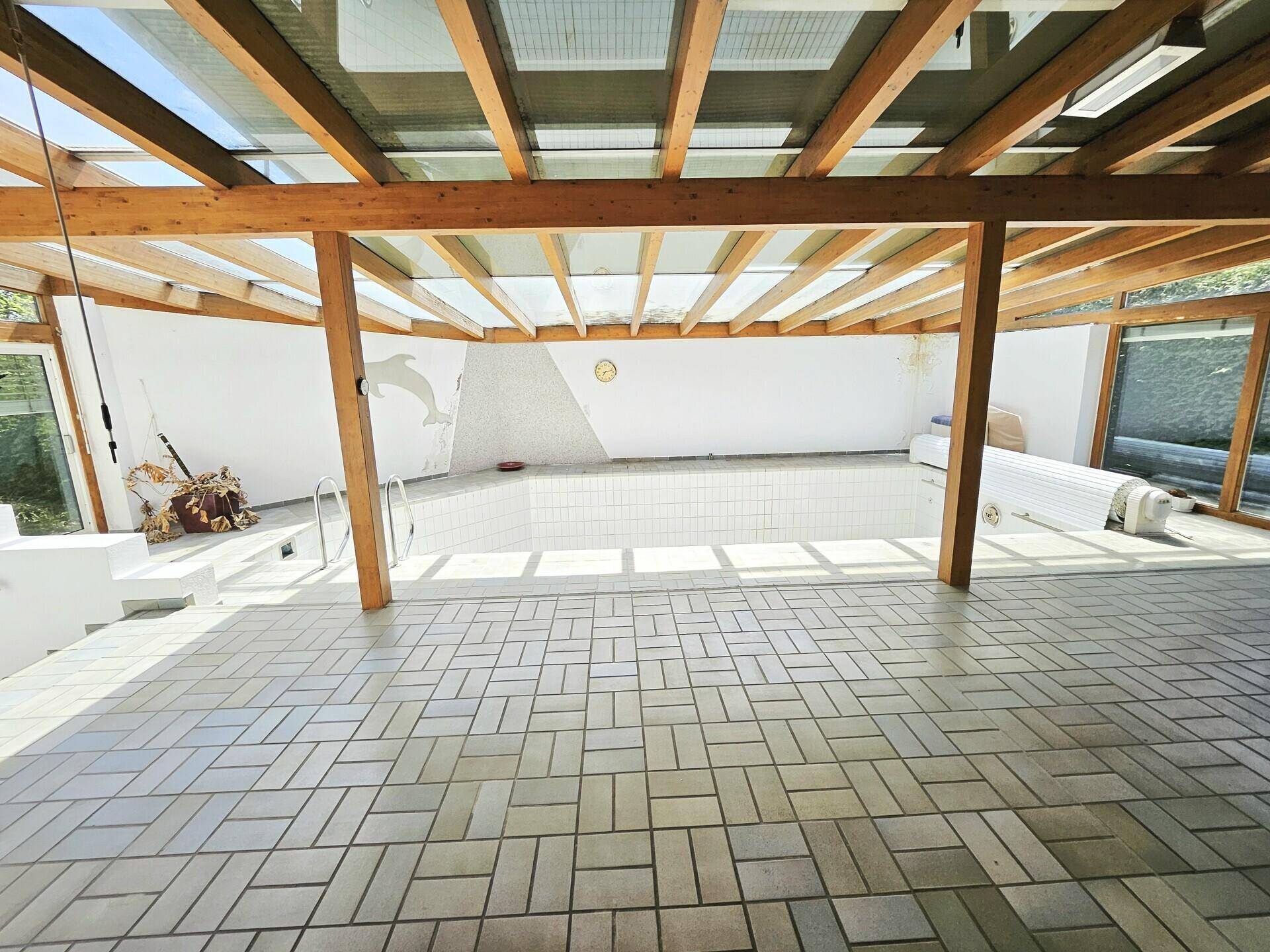 Heller Innenpoolbereich mit Glasdach und gefliestem Boden, ideal zum Entspannen.