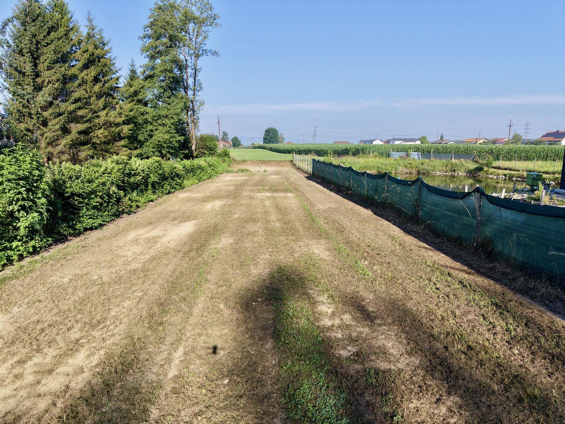 Vorbereiteter Grundstücksstreifen mit Blick auf angrenzende Felder und Siedlungsgebiet in der Ferne.