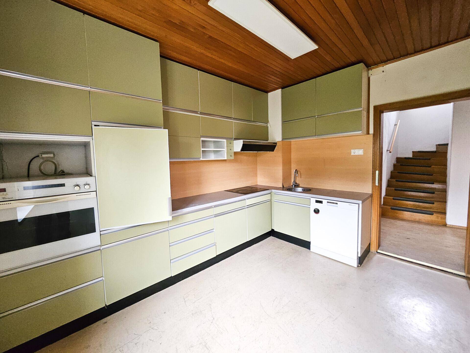 Küche im Retro-Stil mit grünen Schränken, Holzdecke und integrierten Geräten.
