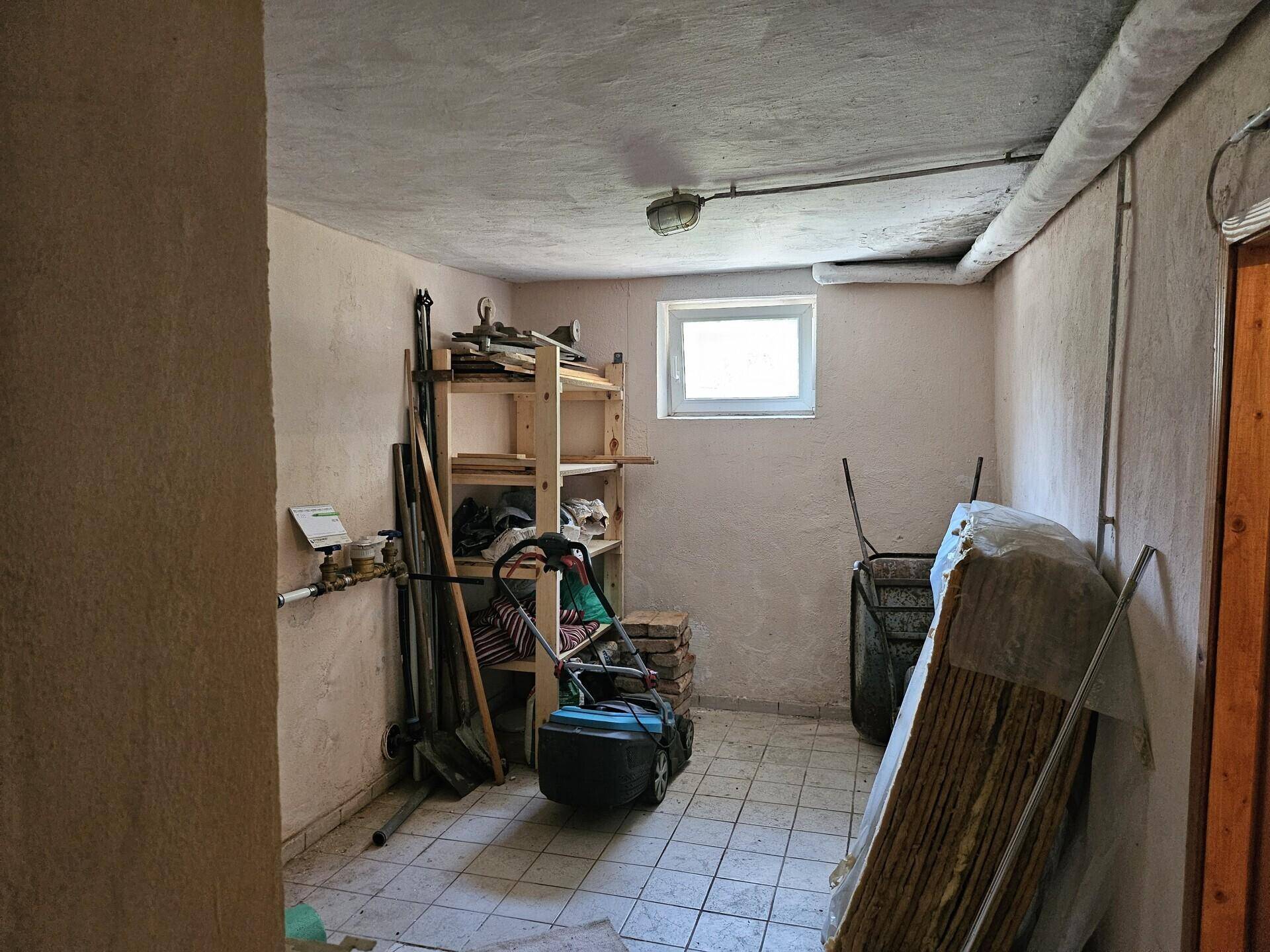 Gefliester Kellerraum mit Regalen, kleinem Fenster und sichtbaren Installationen, als Lagerraum genutzt.