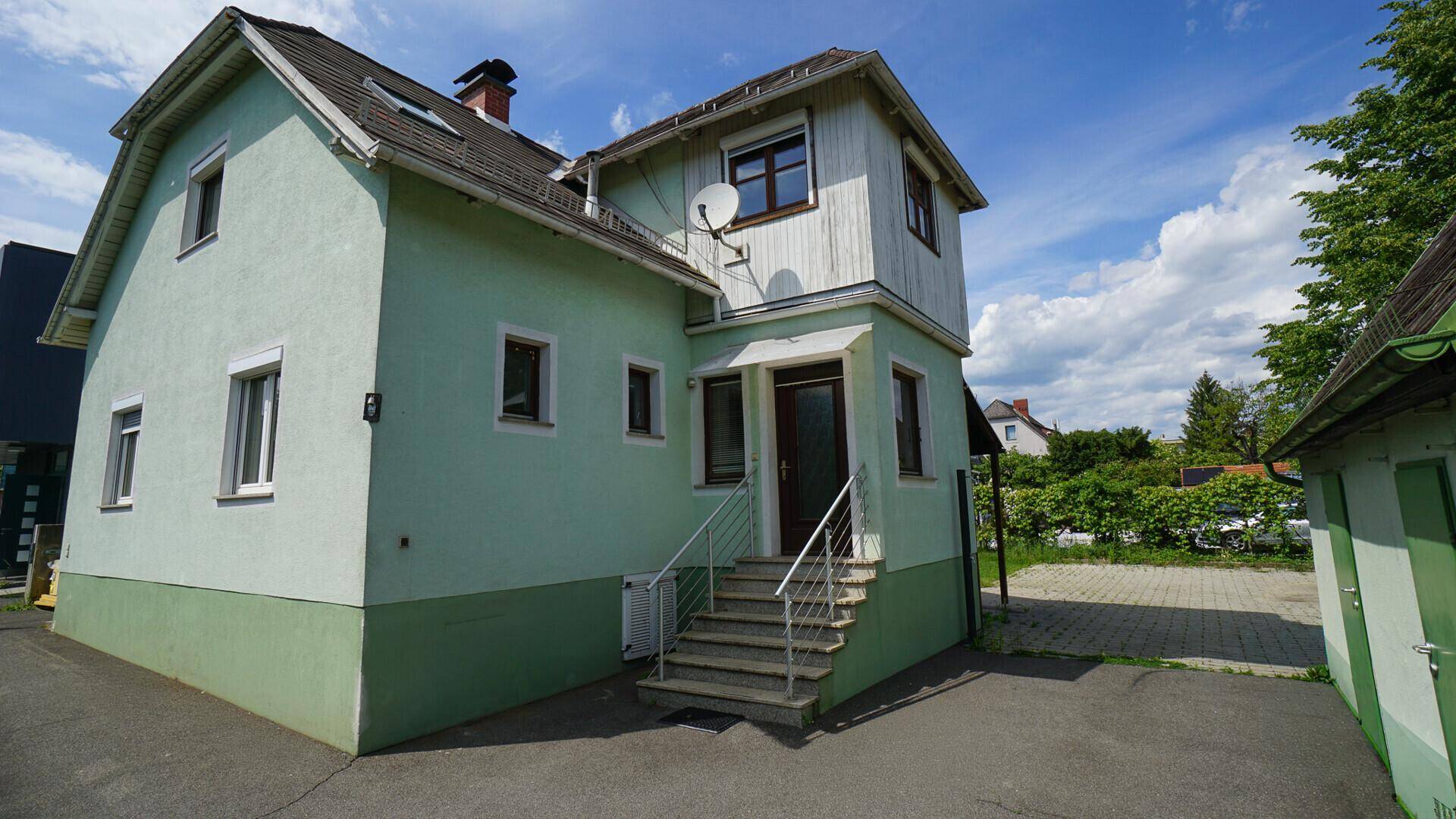 Hellgrünes Wohnhaus mit Eingangsbereich und Treppe, umgeben von viel Grün.