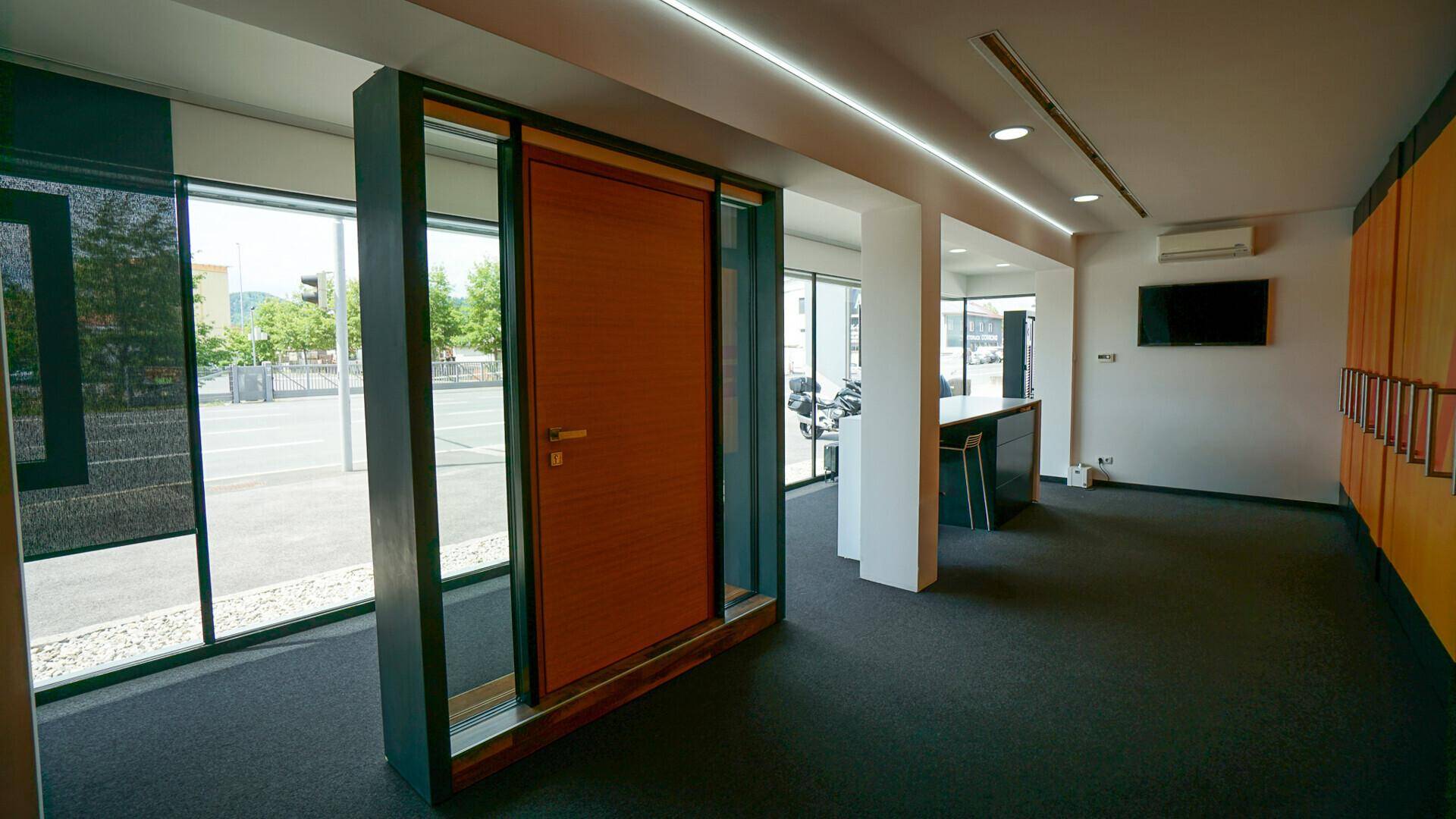 Heller Ausstellungsraum mit Teppichboden, modernen Leuchten und einer präsentierten Holztür.