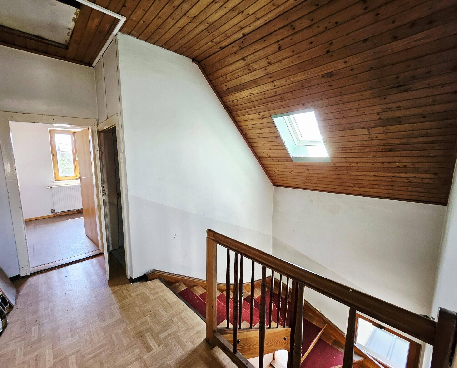 Treppenaufgang mit Holzdecke und Dachfenster, das den Bereich erhellt.