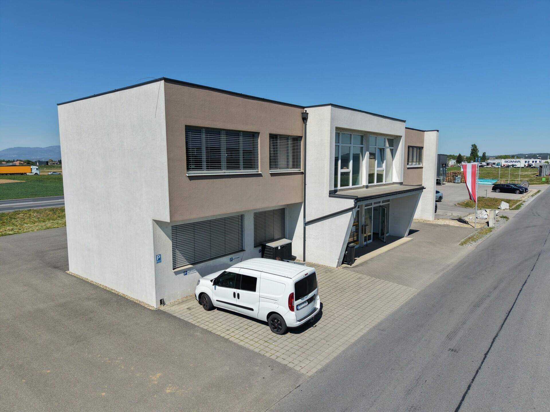 Ansicht eines modernen Geschäftsgebäudes mit weißer und beiger Fassade und gepflastertem Vorplatz.