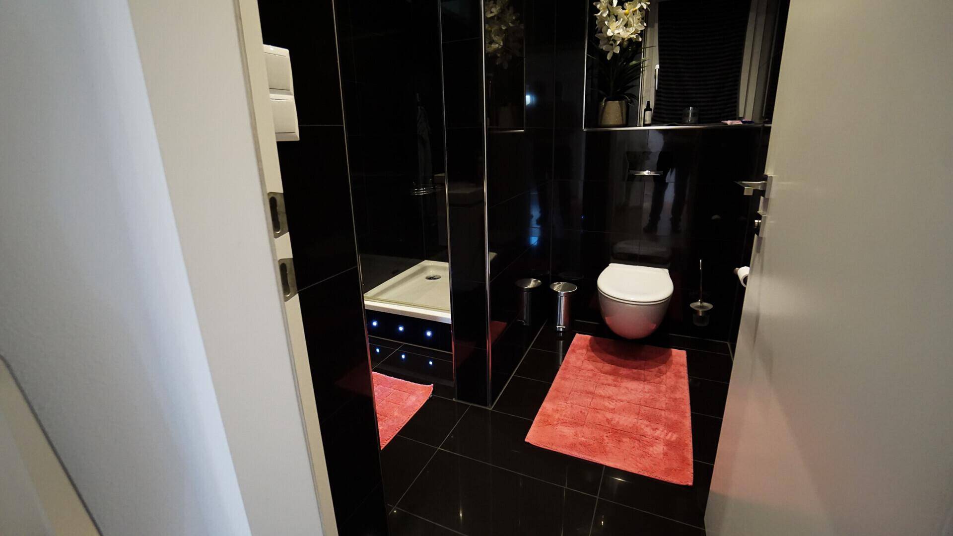 Elegantes Badezimmer mit schwarzen Hochglanzfliesen, moderner Dusche und Wand-WC.