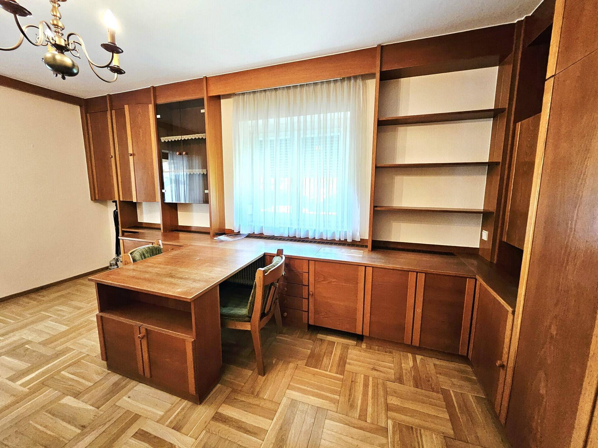 Arbeitszimmer mit Einbauschränken aus Holz, Schreibtisch und Parkettboden.