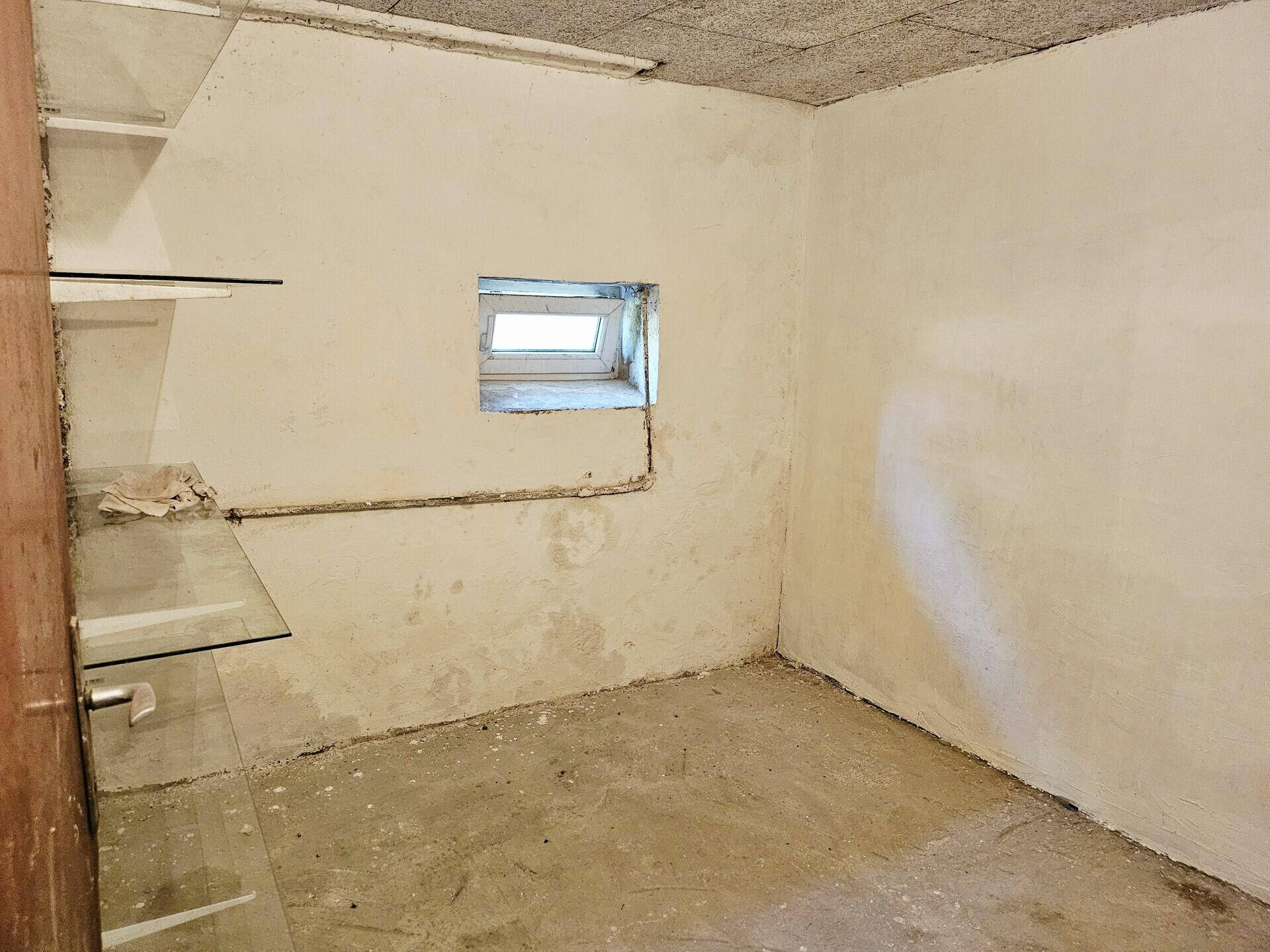 Kleiner, leerer Kellerraum mit einem hochgelegenen Fenster und Betonboden, als Abstellraum geeignet.