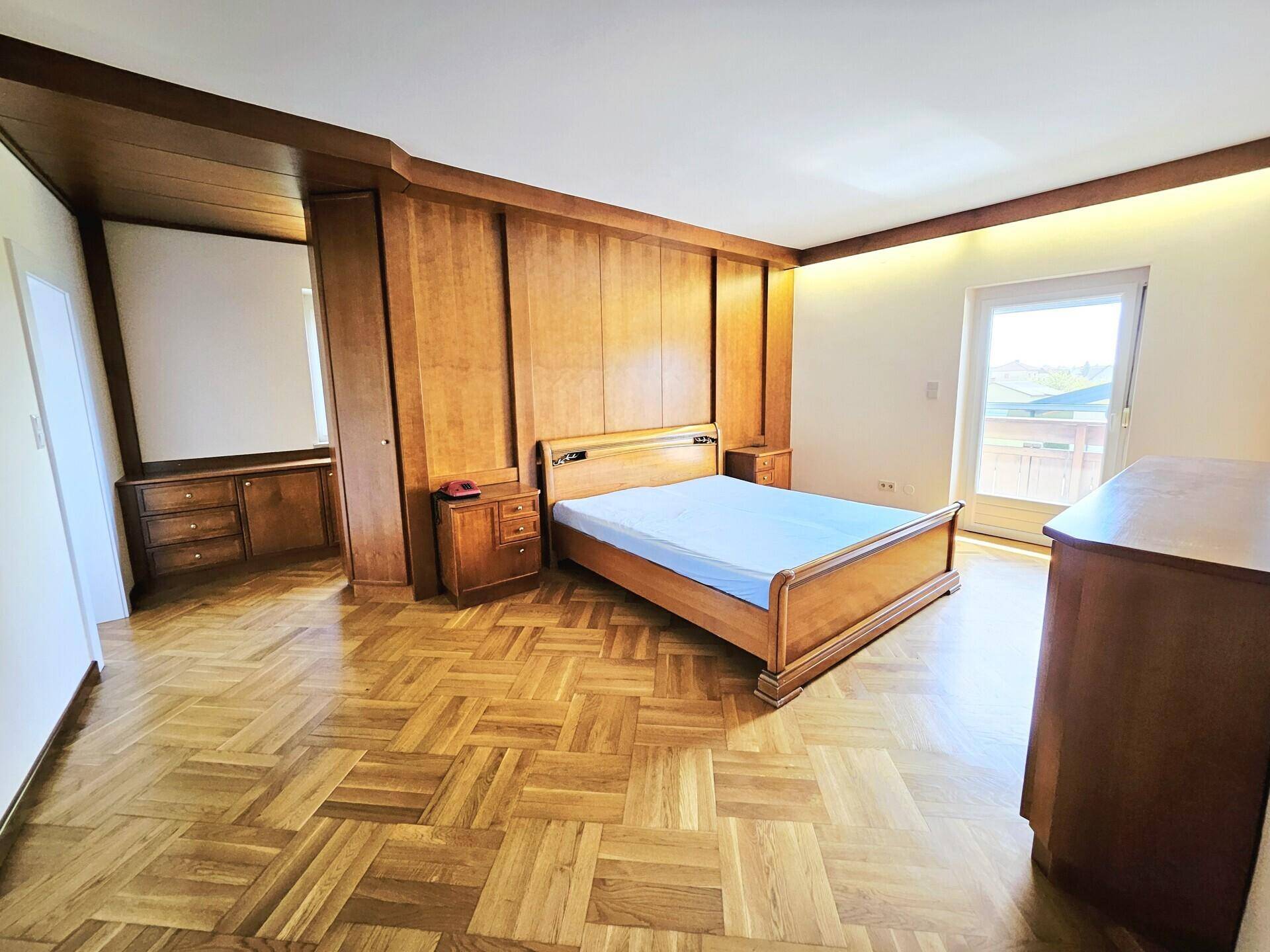 Hauptschlafzimmer mit Parkettboden, integriertem Holz-Kopfteil und Zugang zum Balkon.