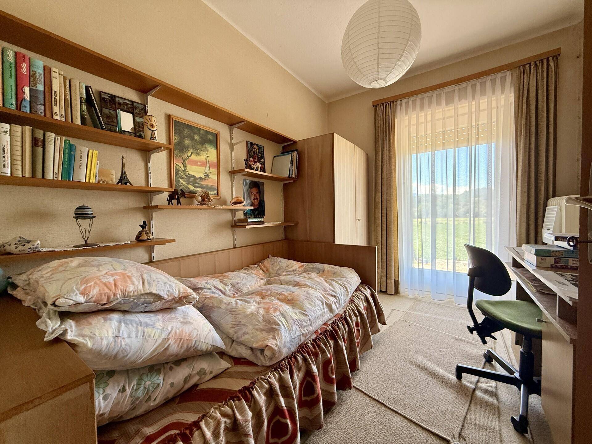 Kinder- oder Gästezimmer mit Einzelbett, Schreibtisch und Regalen, hell und funktional.