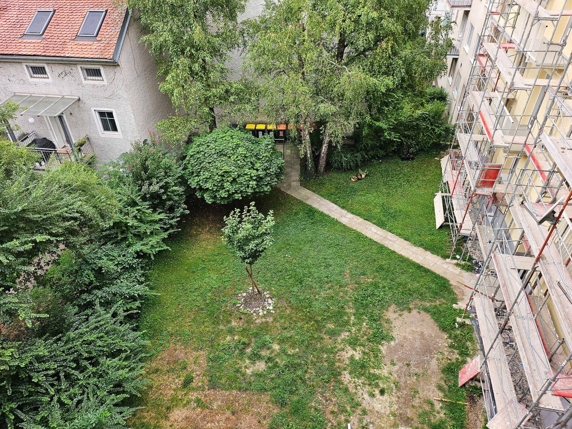 Blick von oben auf einen grünen Innenhof mit Rasenfläche und Bäumen, umgeben von Gebäuden.