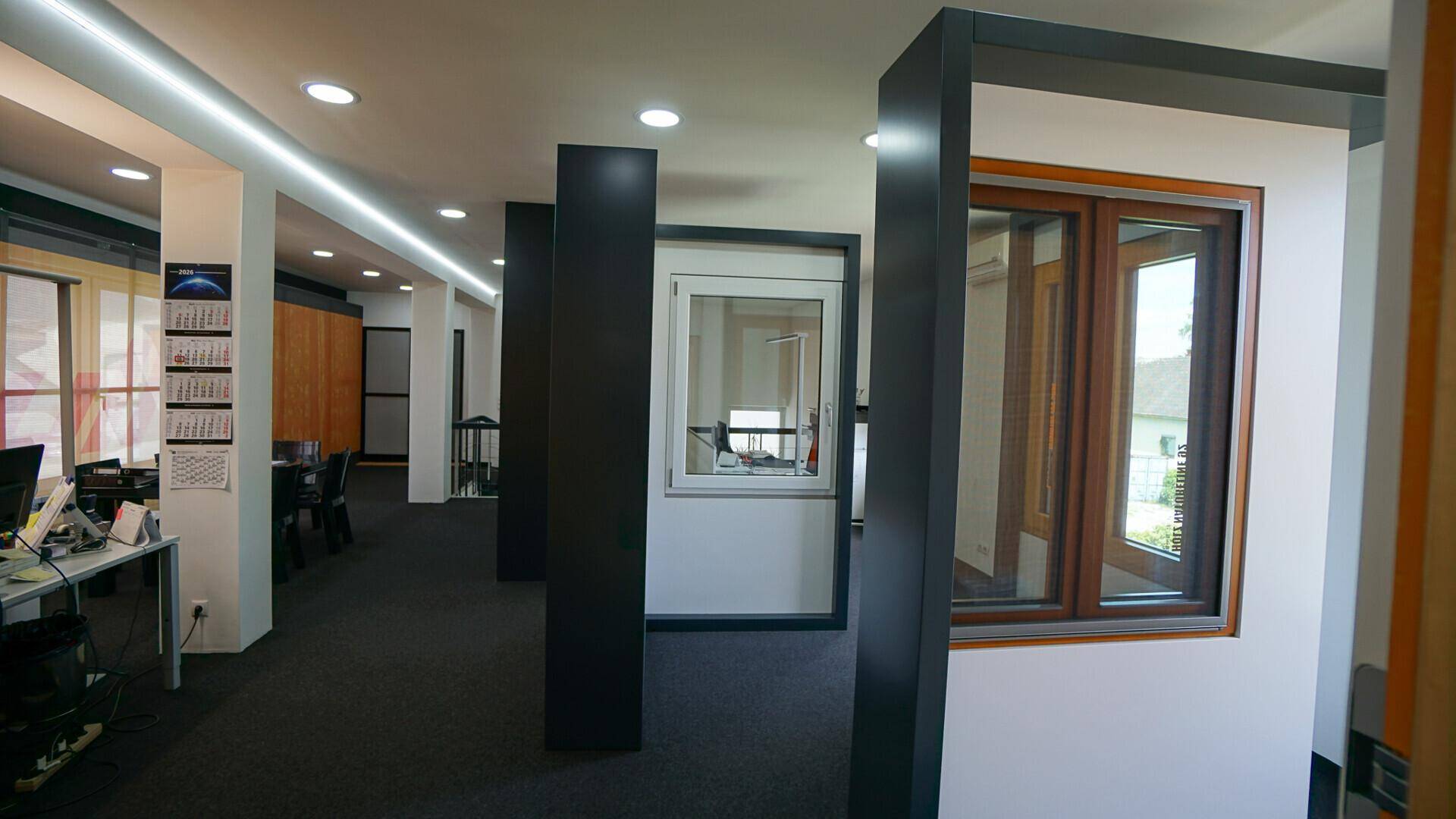 Heller Ausstellungsraum mit verschiedenen Fenstermodellen und dunklem Teppichboden.