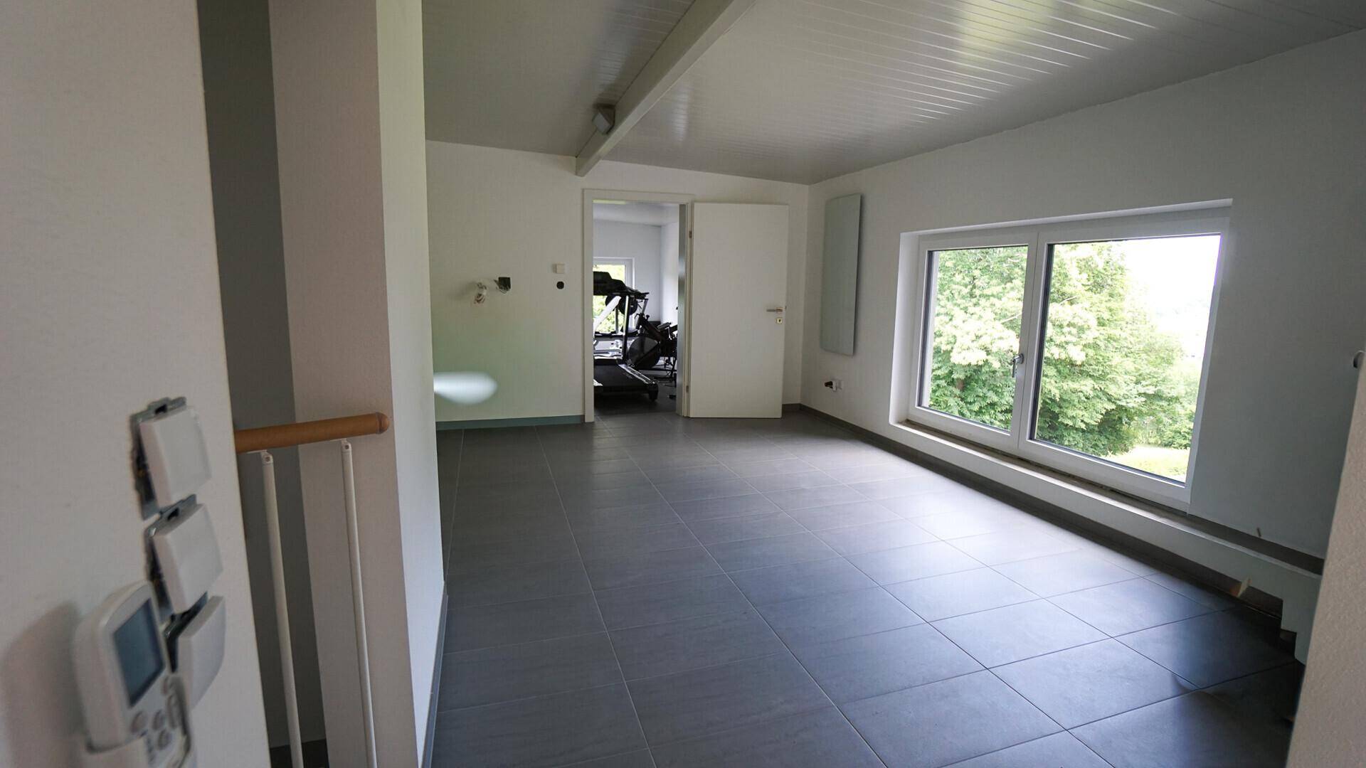 Heller Flur mit modernen grauen Fliesen und Blick ins Grüne durch große Fenster.