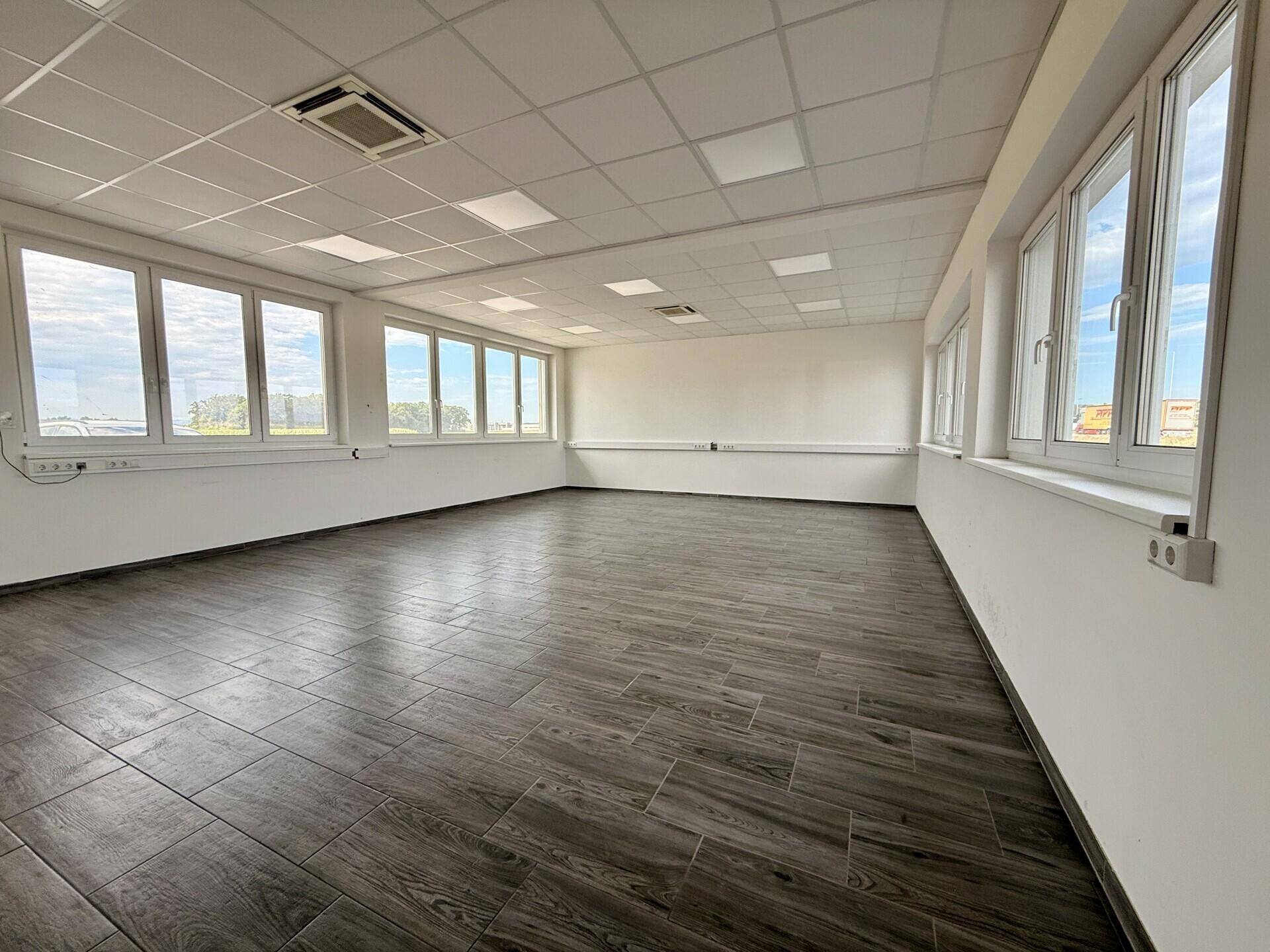 Helles, geräumiges Zimmer mit vielen Fenstern, dunklem Fliesenboden und abgehängter Decke.