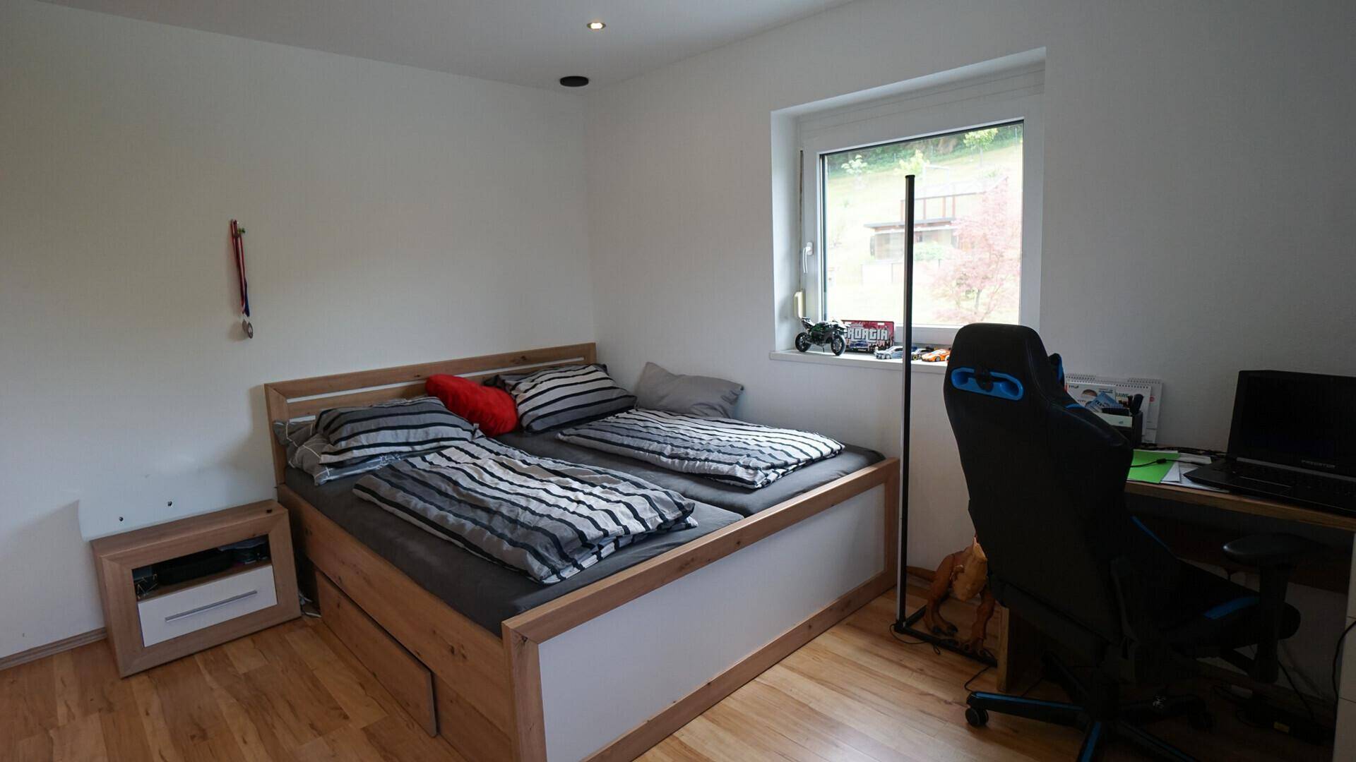 Modernes Schlafzimmer mit Holzbett, Schreibtisch und einem schönen Blick ins Grüne.