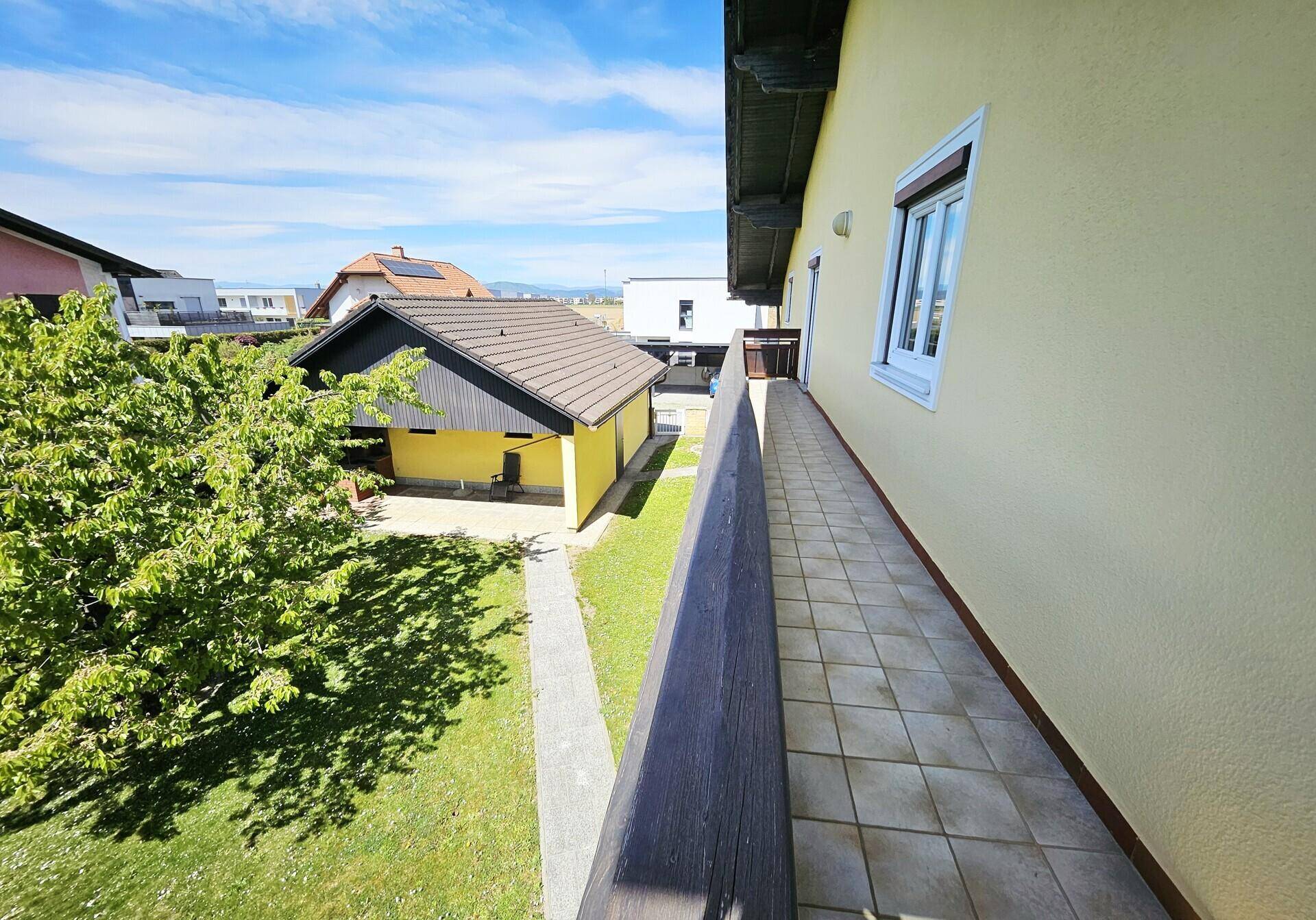 Langer Balkon mit Fliesenboden und Blick auf den Garten und die Umgebung.
