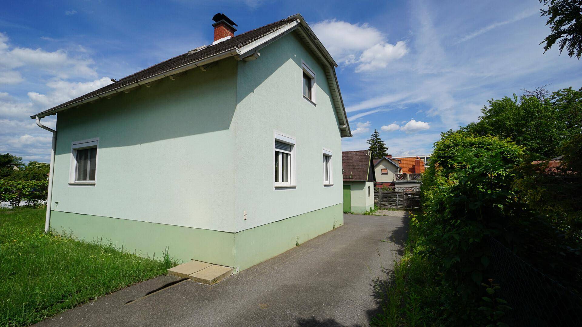 Seitenansicht des hellgrünen Hauses mit Zufahrt und Rasenfläche an einem sonnigen Tag.