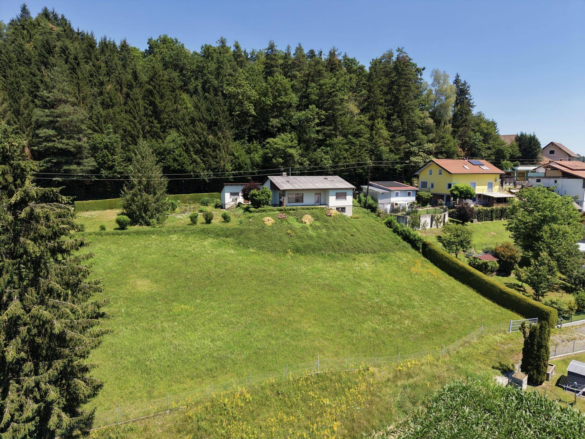 Luftaufnahme des Hauses auf einem Hügel mit weitläufiger Rasenfläche und Wald.
