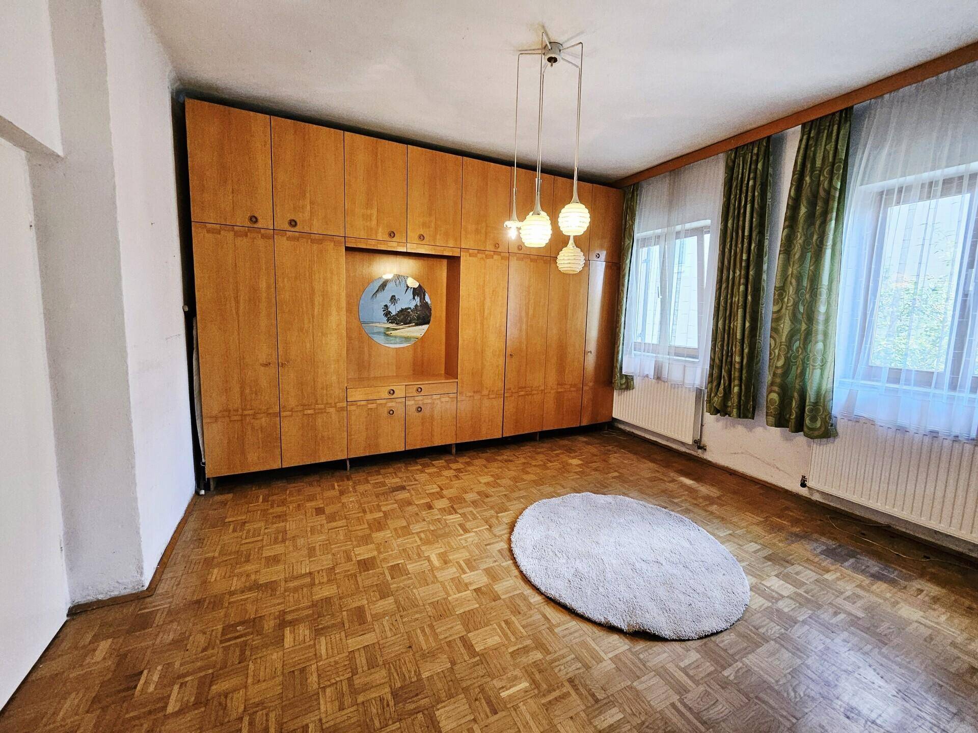 Geräumiges Zimmer mit Parkettboden, großer Einbauschrankwand und zwei Fenstern.