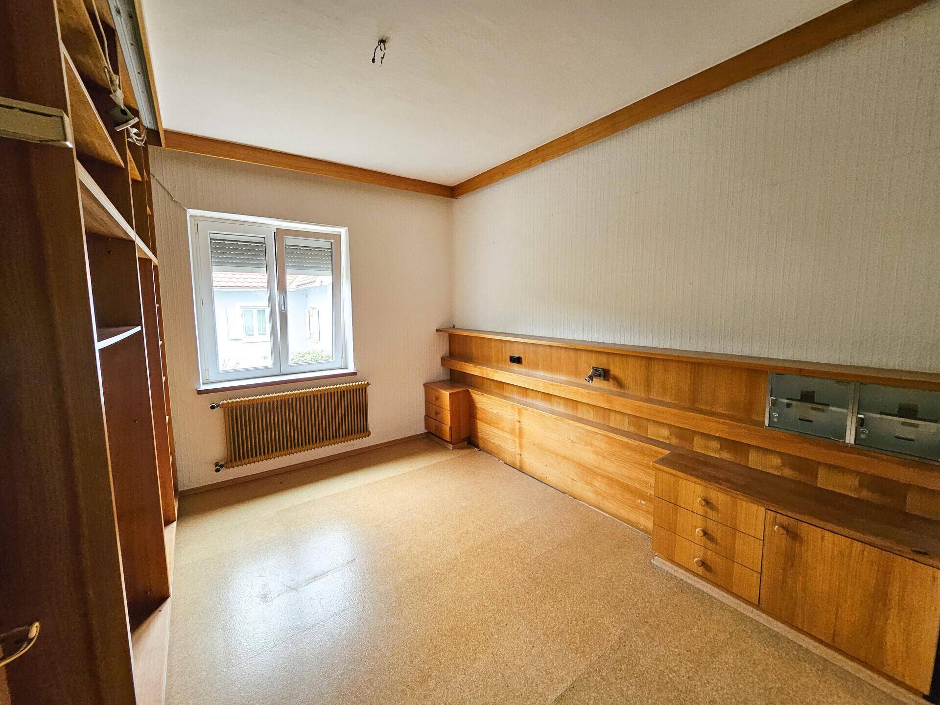 Schlafzimmer mit Korkboden, Einbauregalen und Fenster mit Blick ins Grüne.