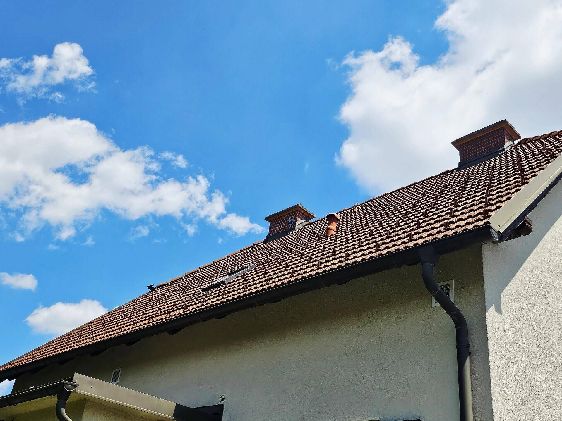 Detailansicht des Ziegeldachs mit Schornsteinen und Dachfenstern unter einem blauen Himmel.