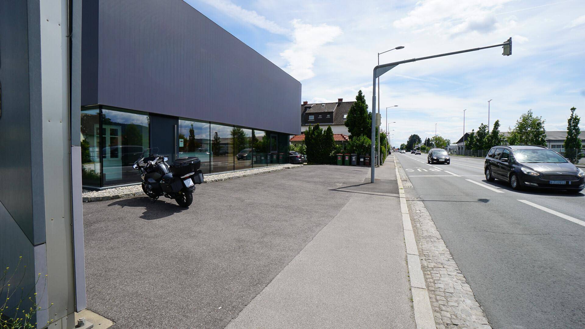 Moderne Geschäftsfassade mit großen Schaufenstern entlang einer belebten Straße an einem sonnigen Tag.