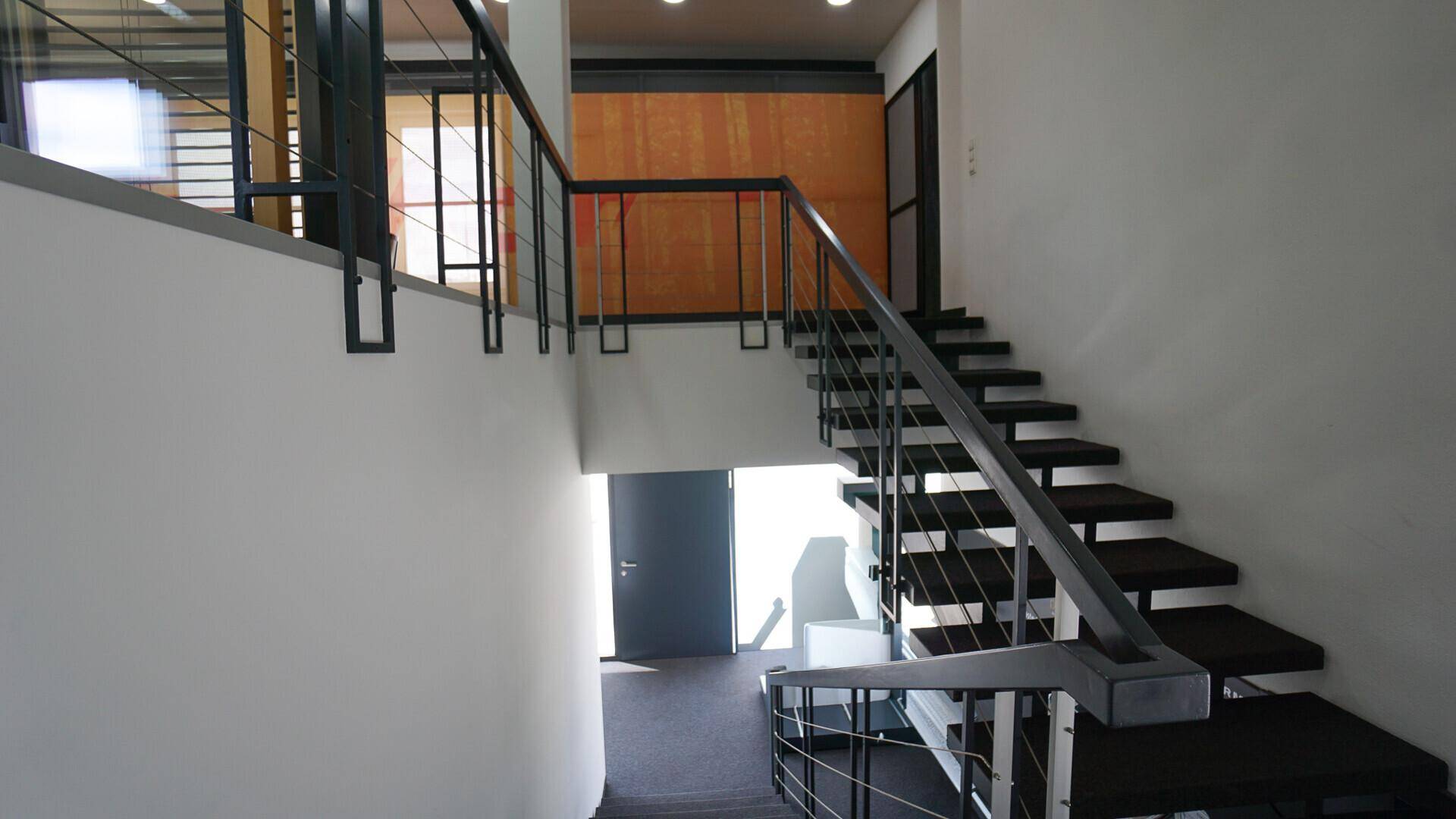 Modernes Treppenhaus mit Metallgeländer und dunklen Stufen, das verschiedene Ebenen verbindet.