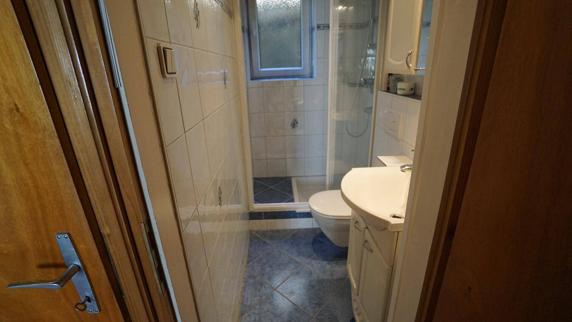 Kleines Badezimmer mit Dusche, WC und Waschbecken, hell gefliest und funktional.