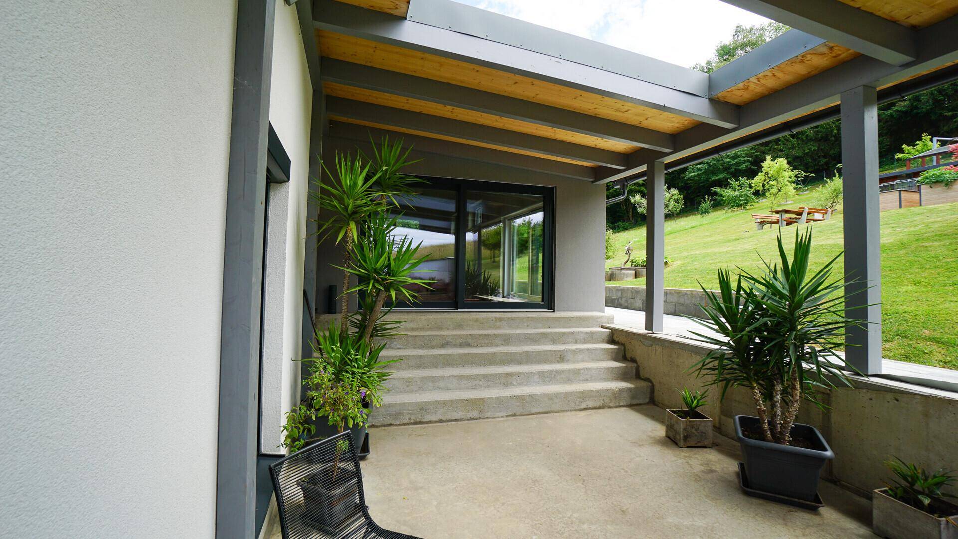 Überdachter Terrassenbereich mit großen Pflanzen und Zugang zum Innenbereich des Hauses.