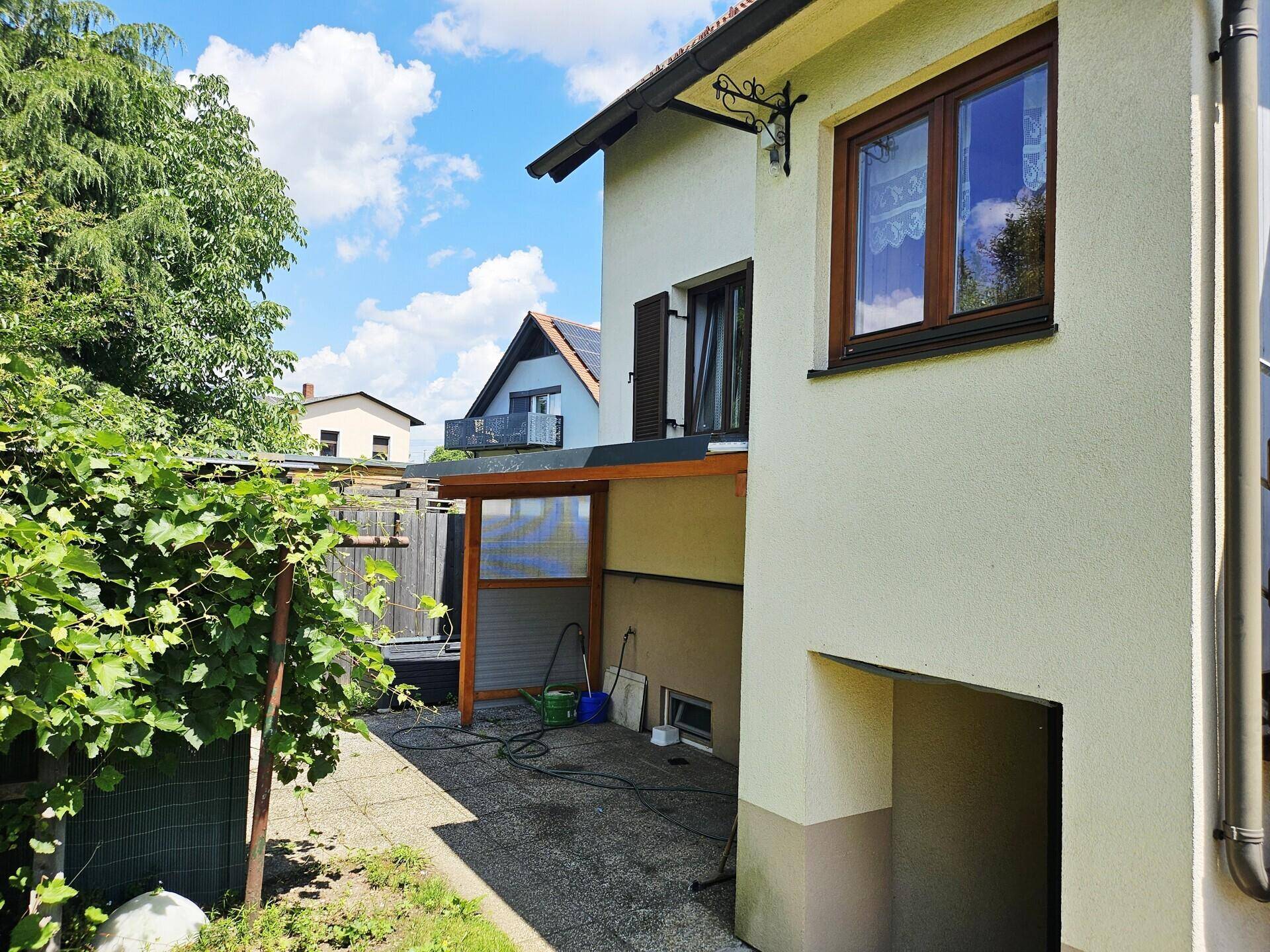 Seitenansicht des Hauses mit überdachtem Bereich und üppiger Vegetation im Garten.